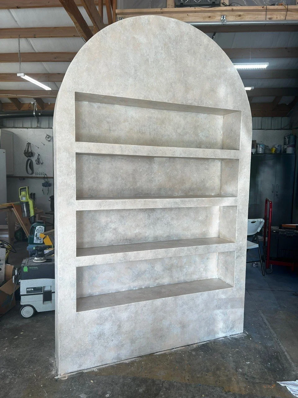 A large, arched concrete or plaster shelf or display unit with five open compartments, standing in a workshop.