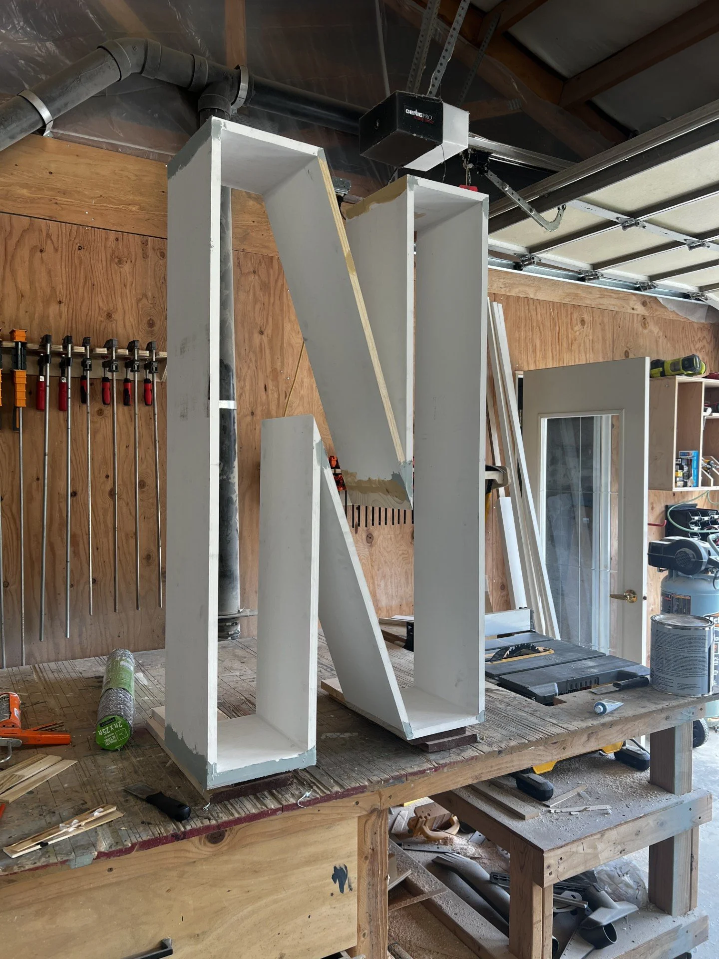 Large white wooden letter N under construction on a workbench in a woodworking shop.