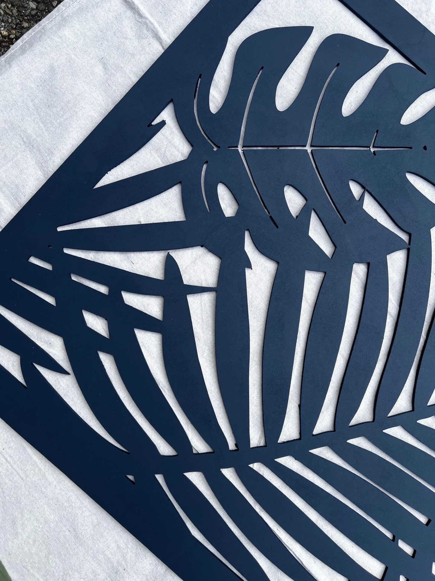 A blue, cut-out metal piece with a tropical leaf pattern, placed on a white surface.