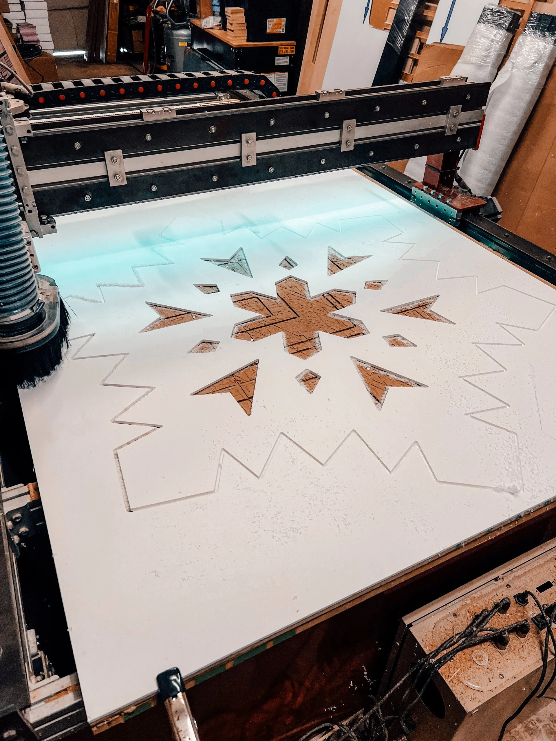 A CNC machine carving a snowflake pattern into a large white sheet of material in a workshop.