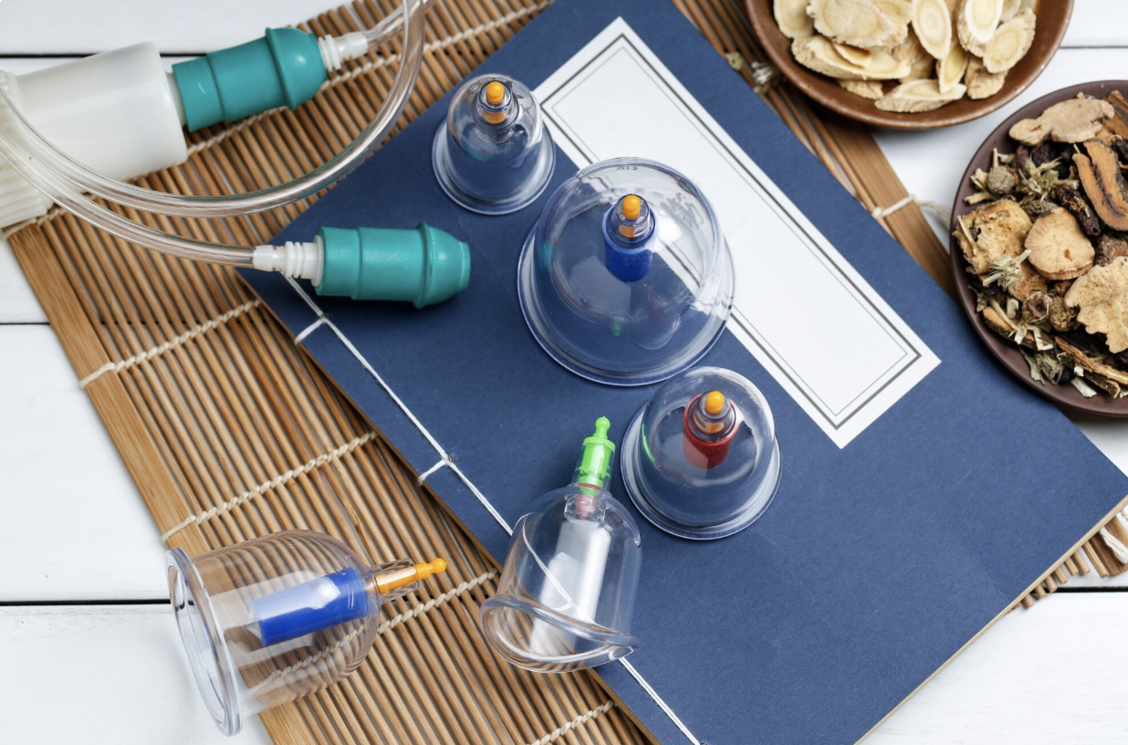 A collection of nasal spray bottles and tips on a desk with plates of dried herbs and roots, a notebook, and a bamboo mat.
