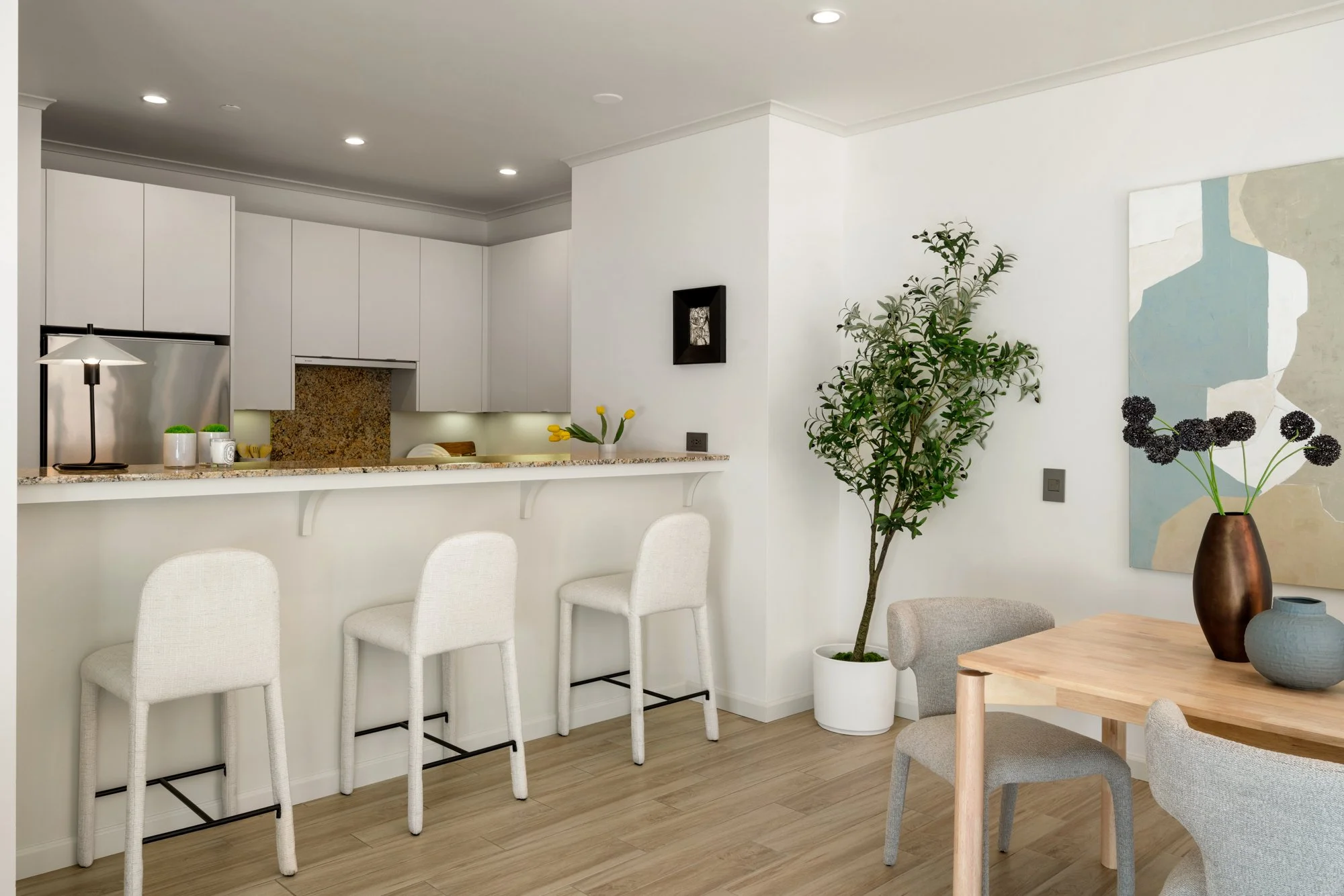 Bright kitchen with white cabinets, a granite countertop breakfast bar with three white chairs, potted plants, modern wall art, and a dining area with a wooden table and gray chairs.
