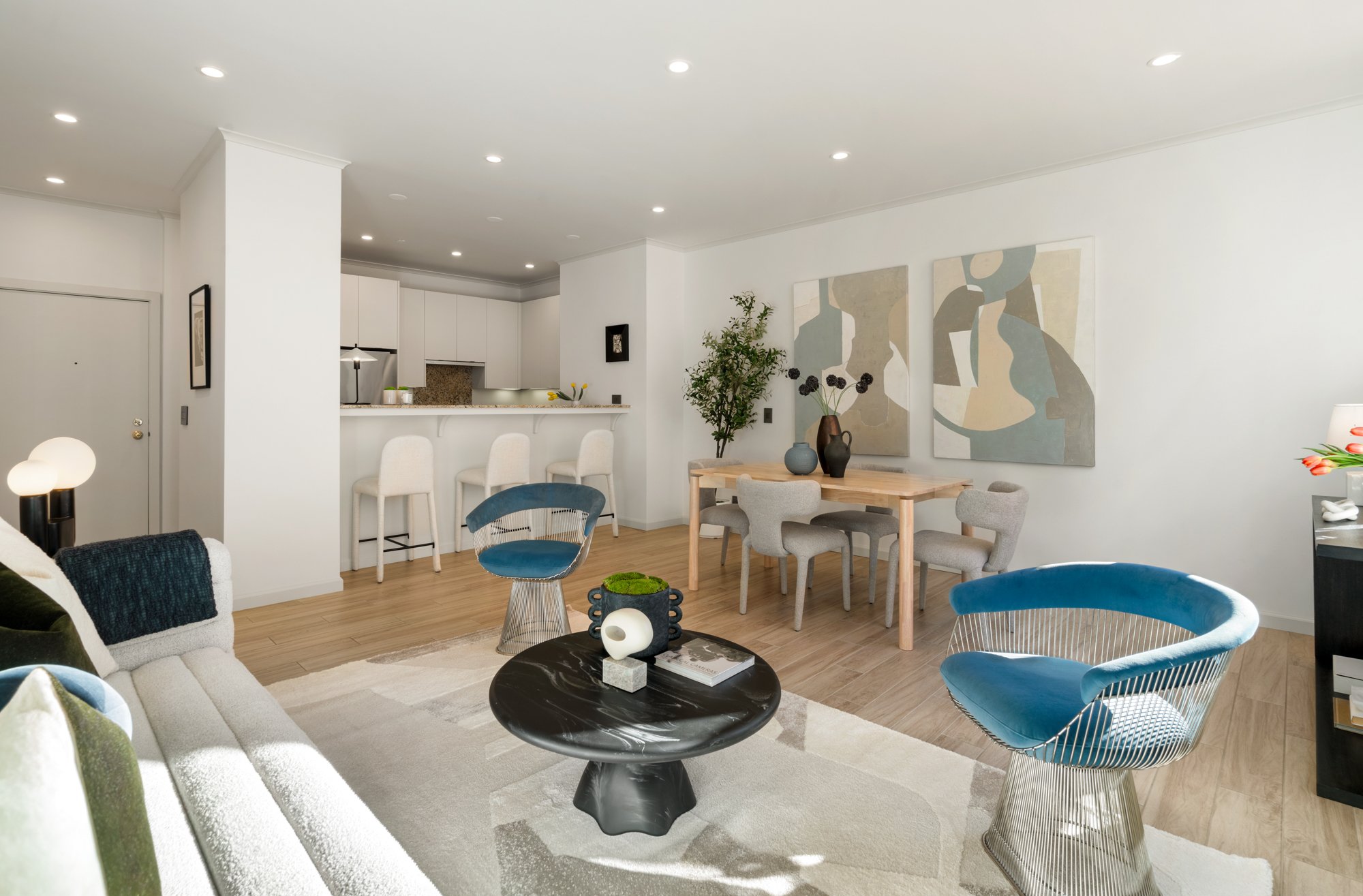 Modern living room and dining area with white walls, light wood flooring, contemporary furniture, and abstract artwork