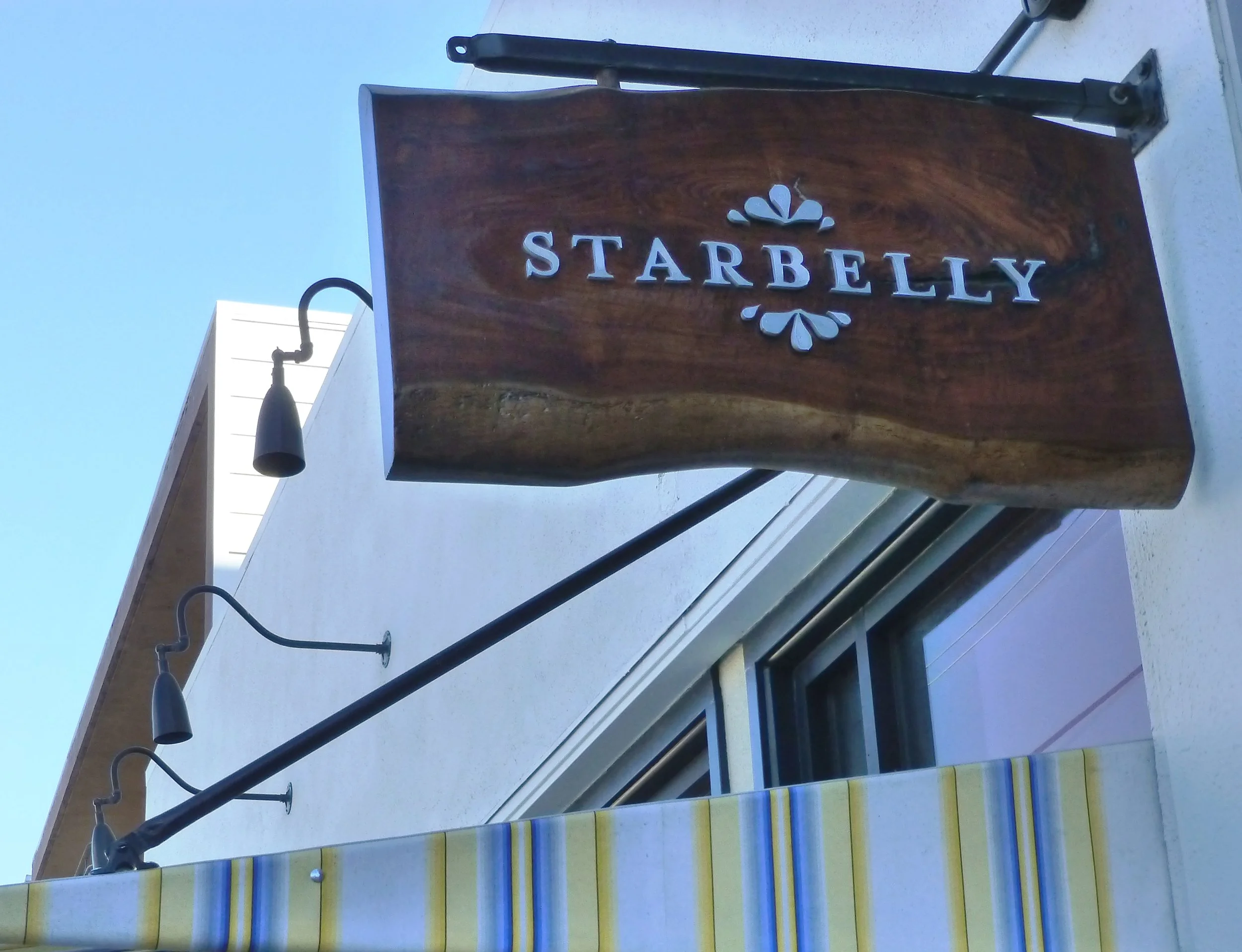 Wooden sign with the word 'Starbelly' in white letters, hanging on a building exterior.