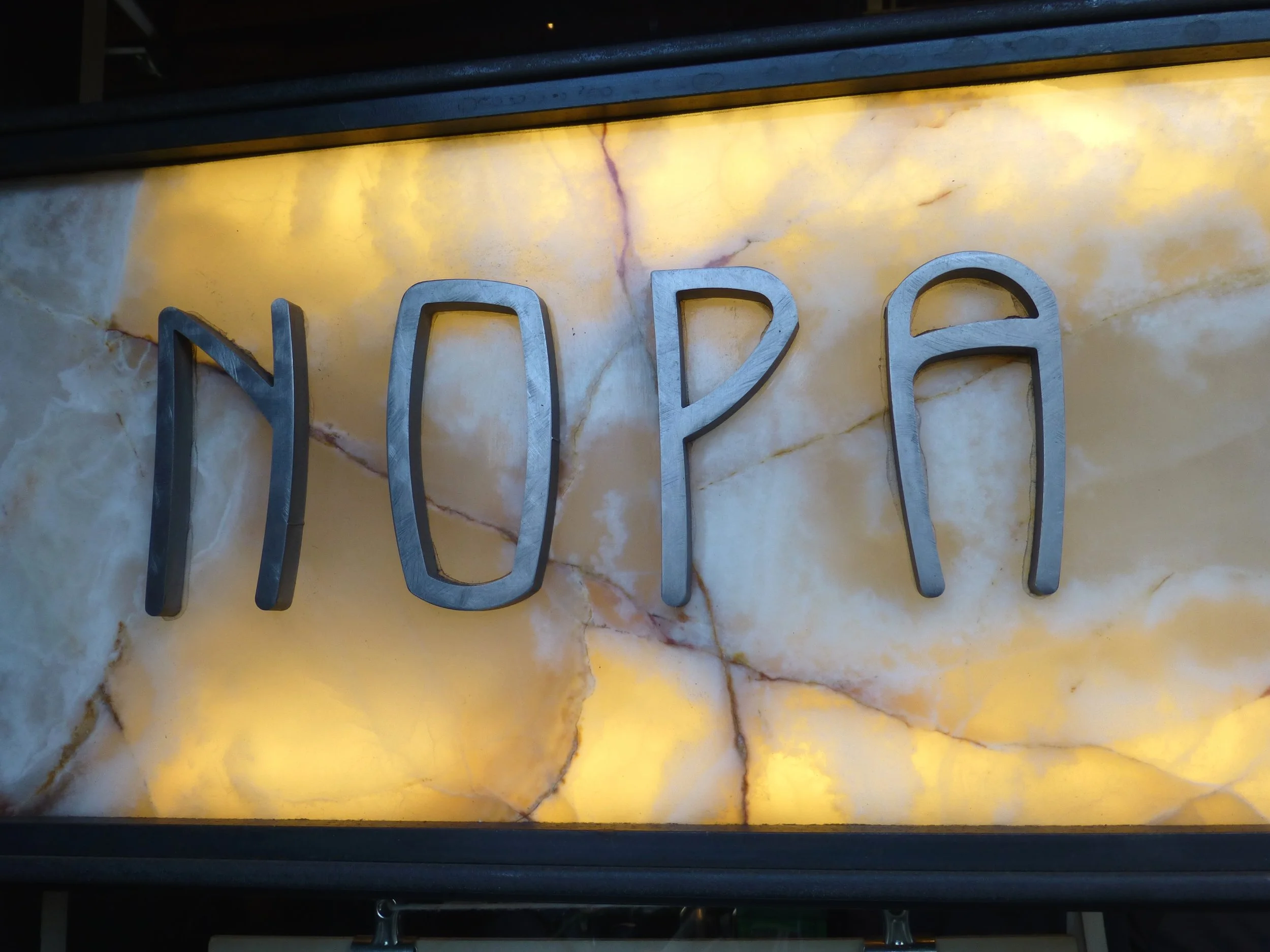 Backlit sign with metal letters spelling 'NOVA' mounted on a marbled yellow and brown wall.
