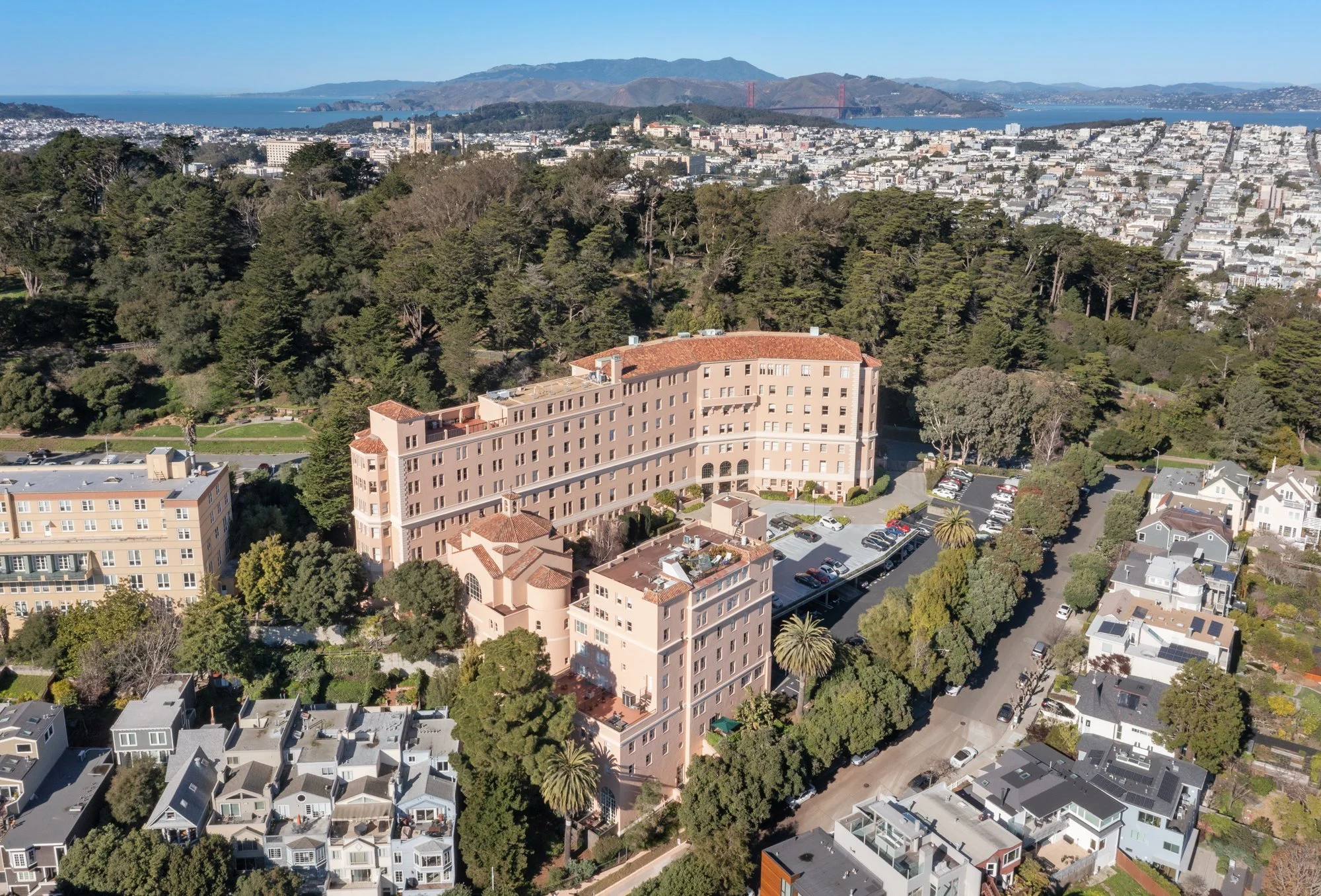 Aerial view of a hotel in San Francisco, with the Golden Gate Bridge and cityscape in the background, surrounded by residential and forested areas.