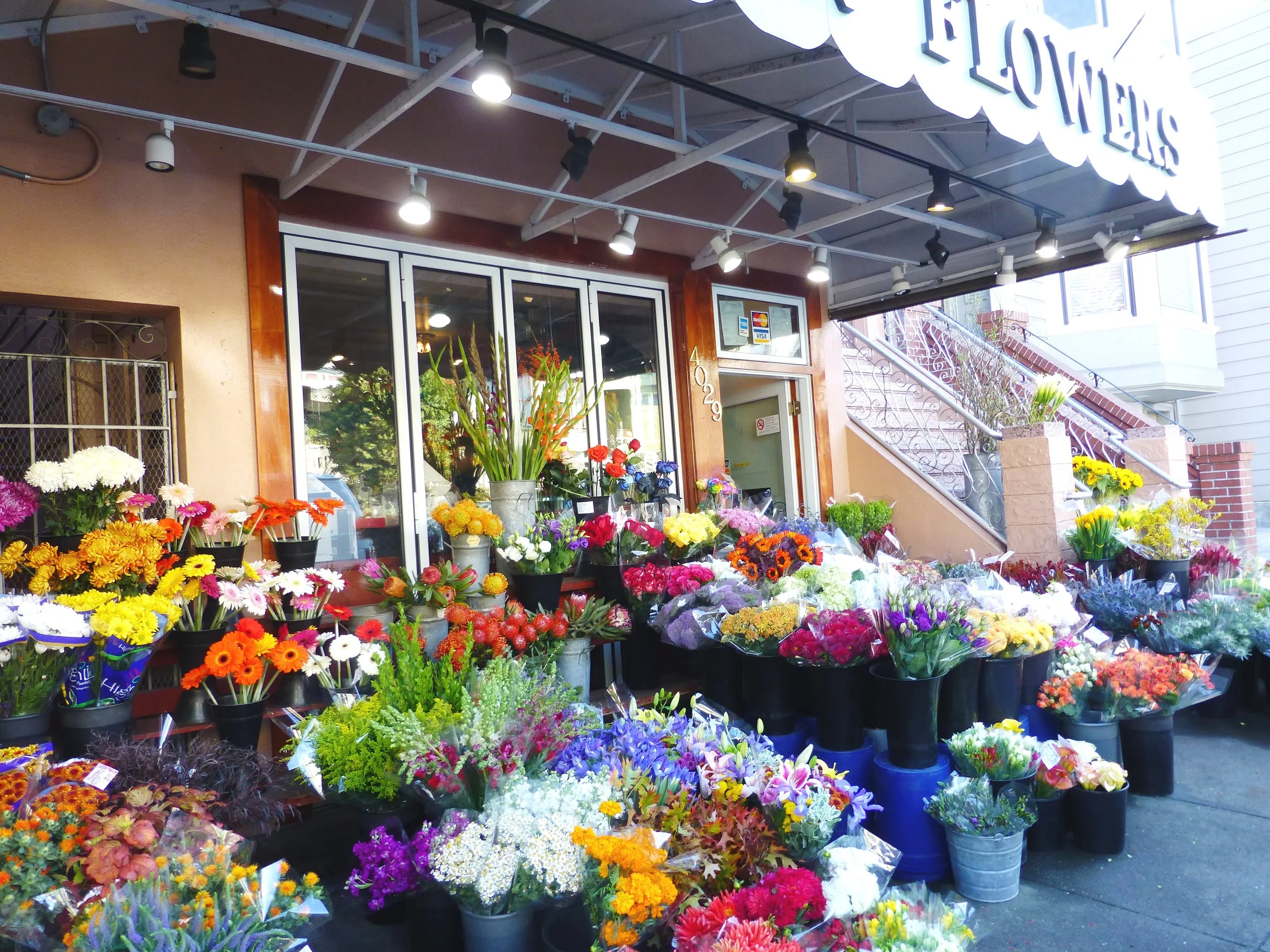 Flower shop with colorful bouquets displayed outside, sign reading 'FLOWERS' on the canopy.
