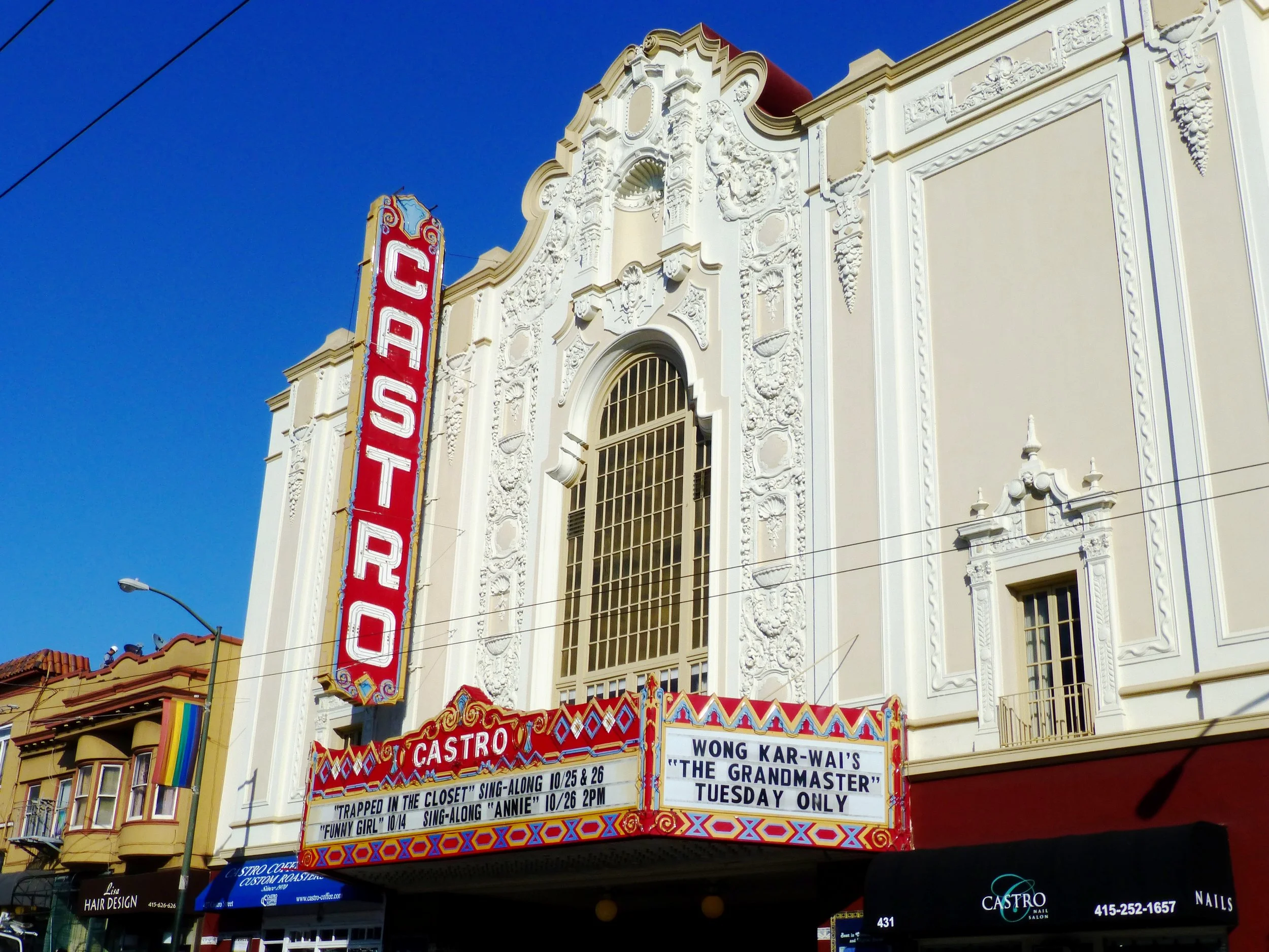 The Castro Theatre, a historic theater with a tall vertical sign reading 'CASTRO' on a decorative facade, features a marquee listing upcoming performances and events, including sing-alongs and a show by Wong Kar-Wai. The building has ornate architect