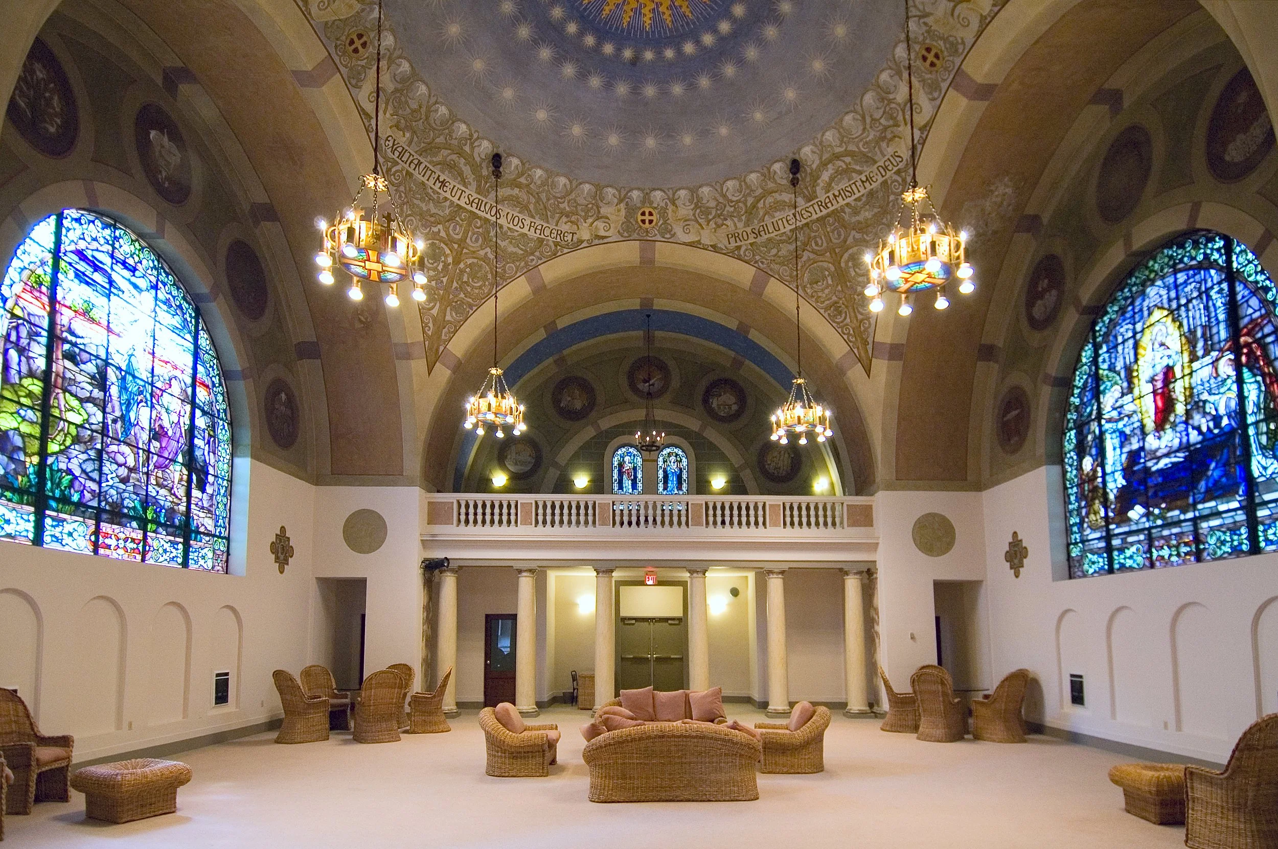 Elegant chapel interior with stained glass windows, chandeliers, and a circular seating arrangement in wicker furniture.