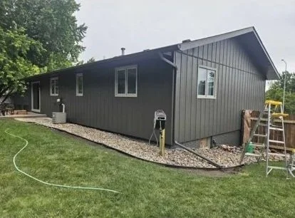 Backyard with a gray house, green grass, tools, and construction materials.
