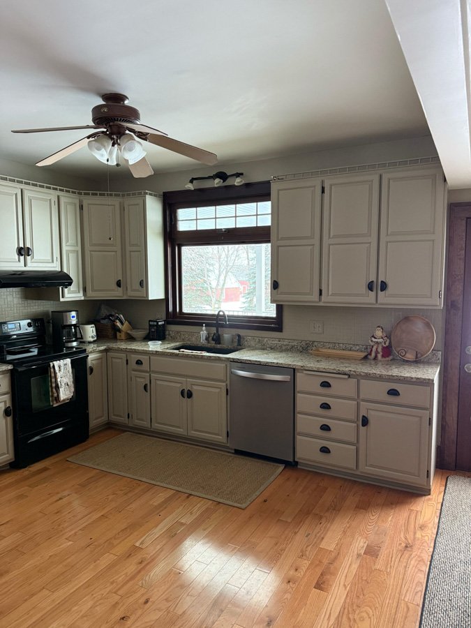 Kitchen with white cabinets, black hardware, granite countertops, a black stove, dish soap, microwave, coffee maker, and a window with a view of a snowy backyard.