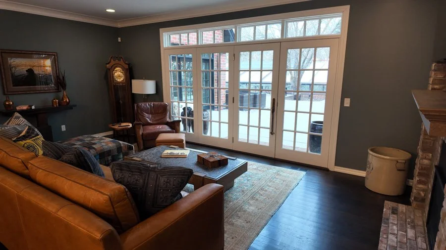 Living room with leather sofa, armchair, coffee table, large glass sliding doors, and a fireplace with brick surround.