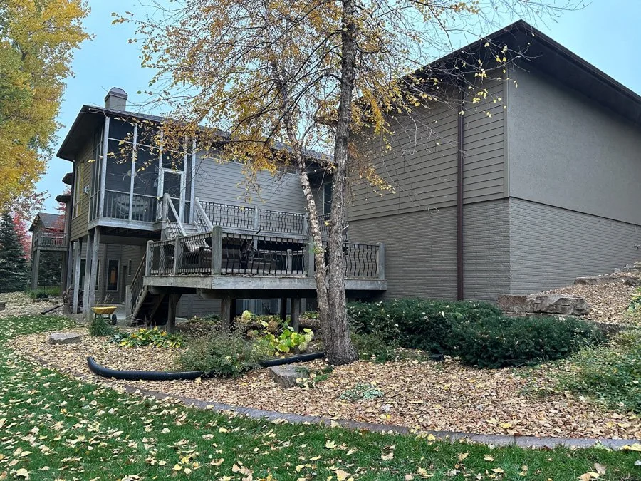 Backyard with a two-story house, trees with fall foliage, a wooden deck, and a landscaped garden.