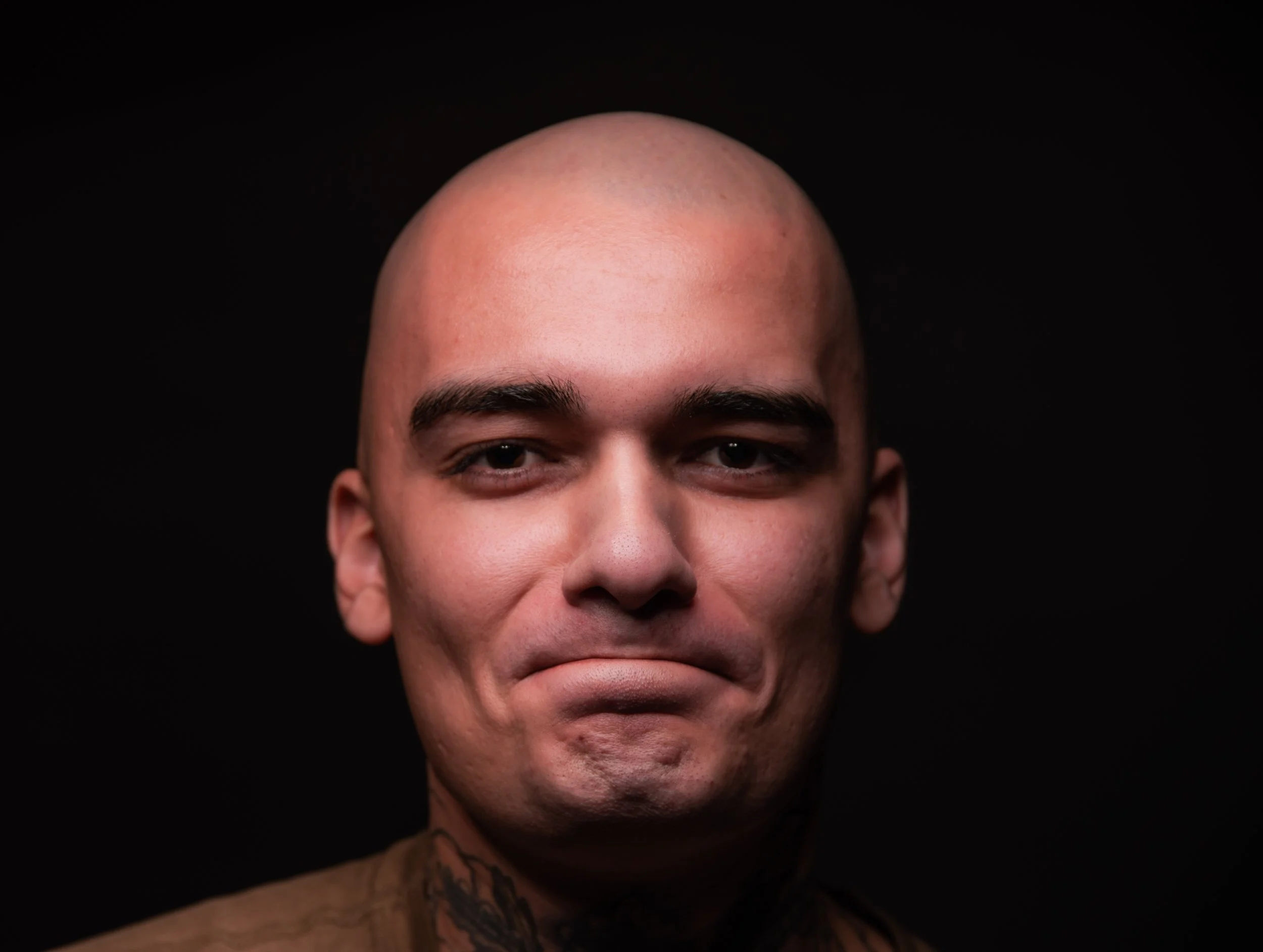 Nahaufnahme eines Mannes mit Glatze vor schwarzem Hintergrund, lächelnd.