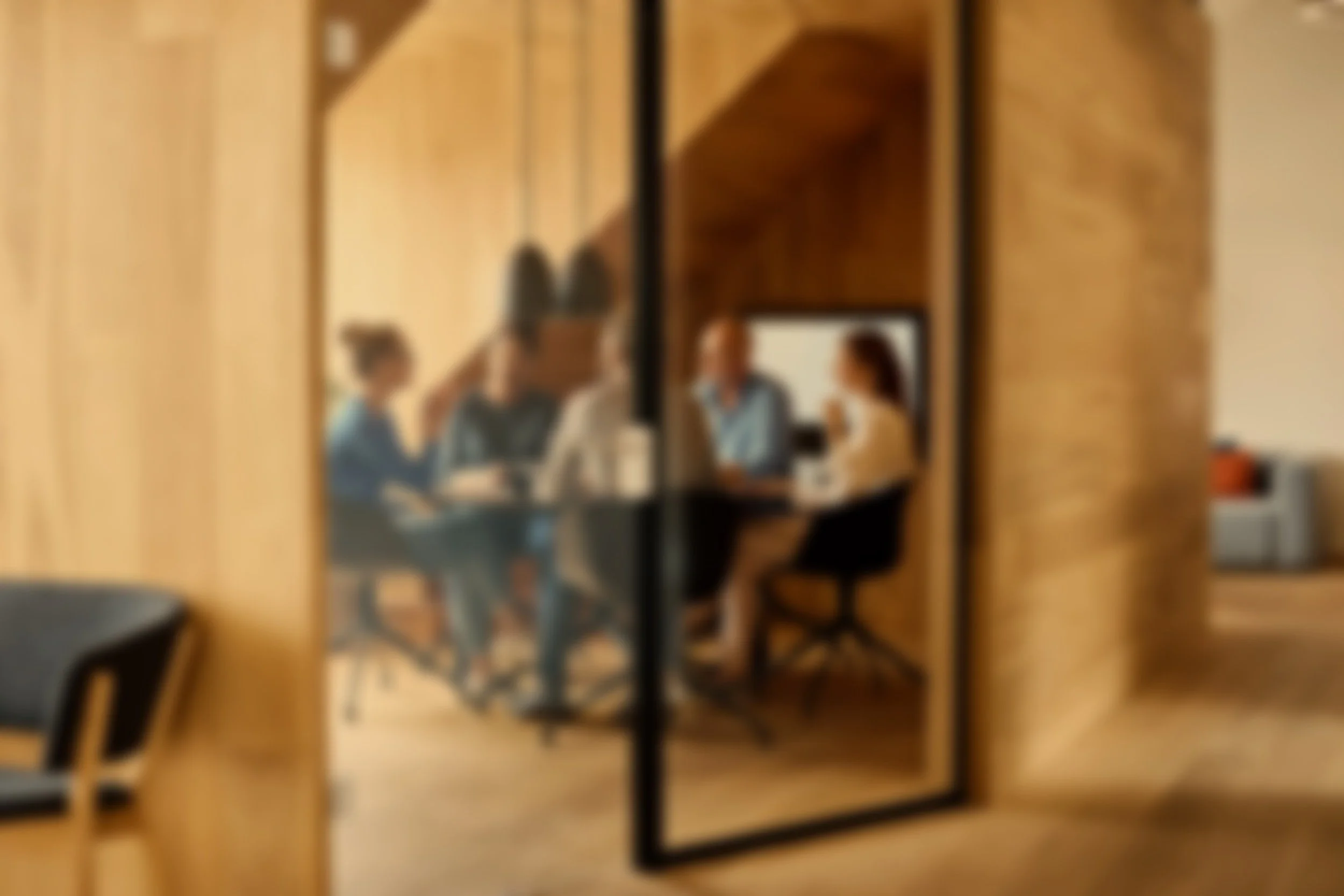 Four people sitting around a table in a private meeting room, viewed through a large mirror in an office or conference space.