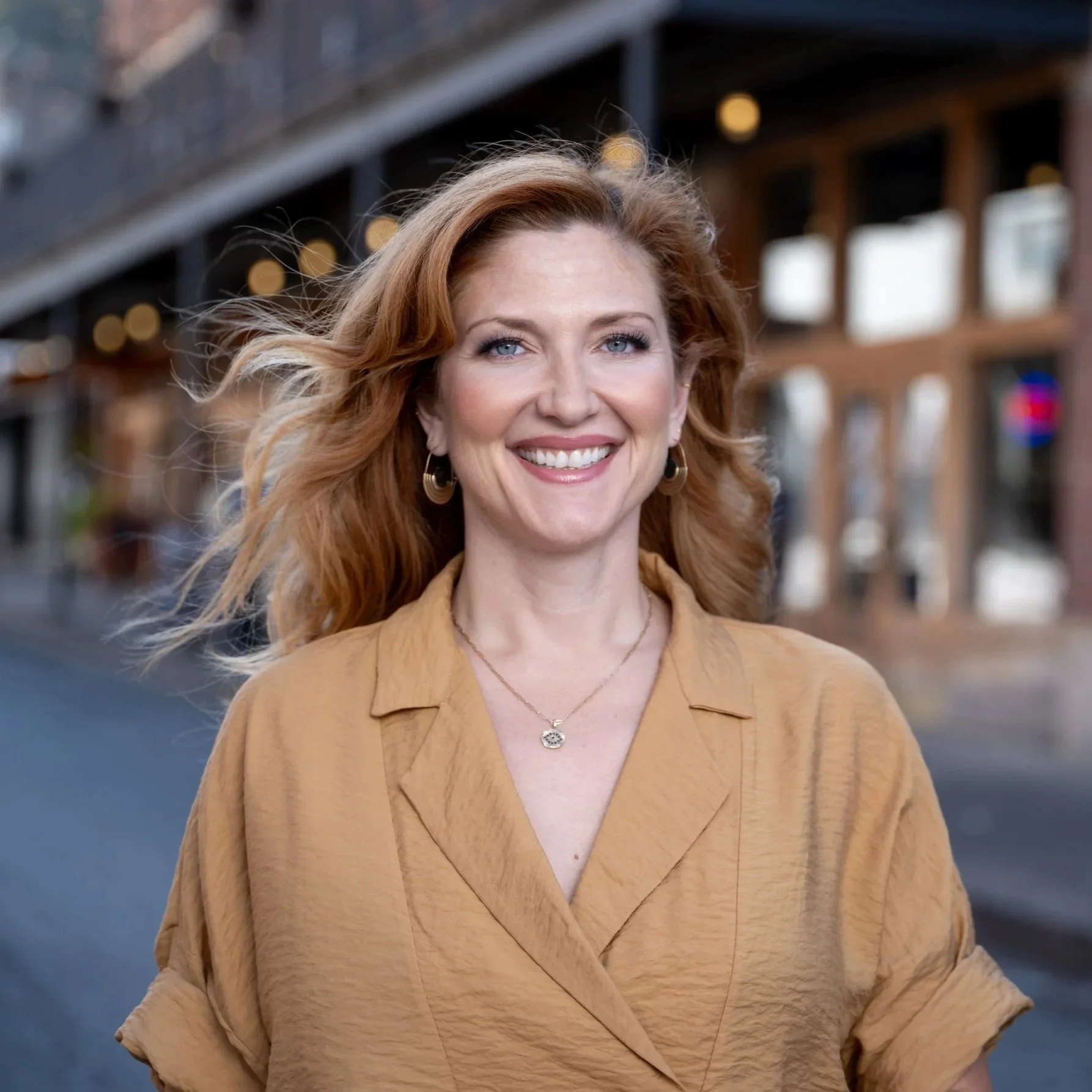 A woman with red hair smiling outdoors on a city street in the Strip District of Pittsburgh.