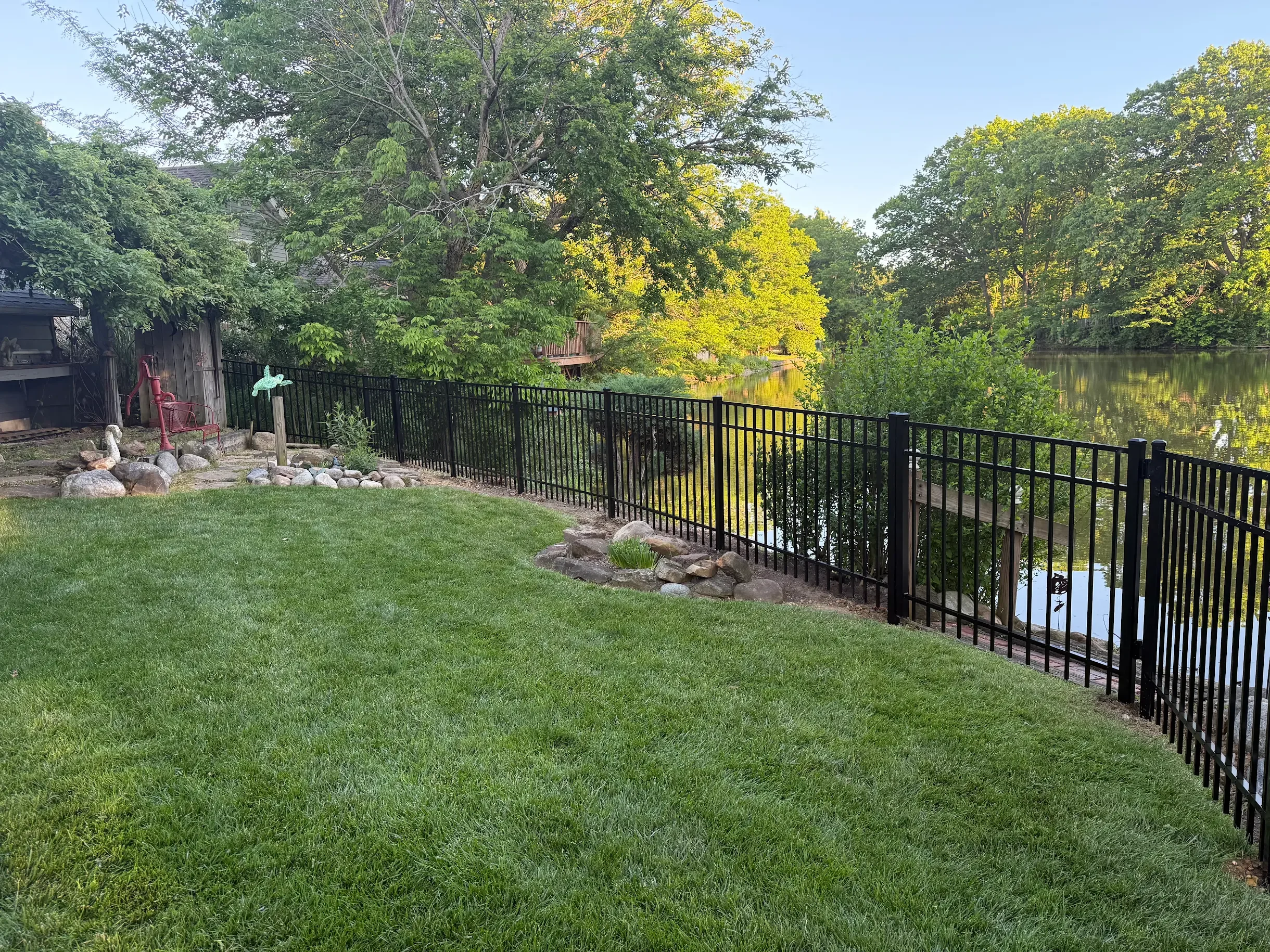 Black aluminum fence around a backyard creating a barrier between the yard and a body of water.