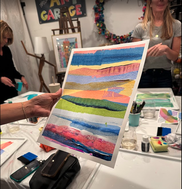 Person holding a colorful abstract landscape watercolor painting in a group art class.