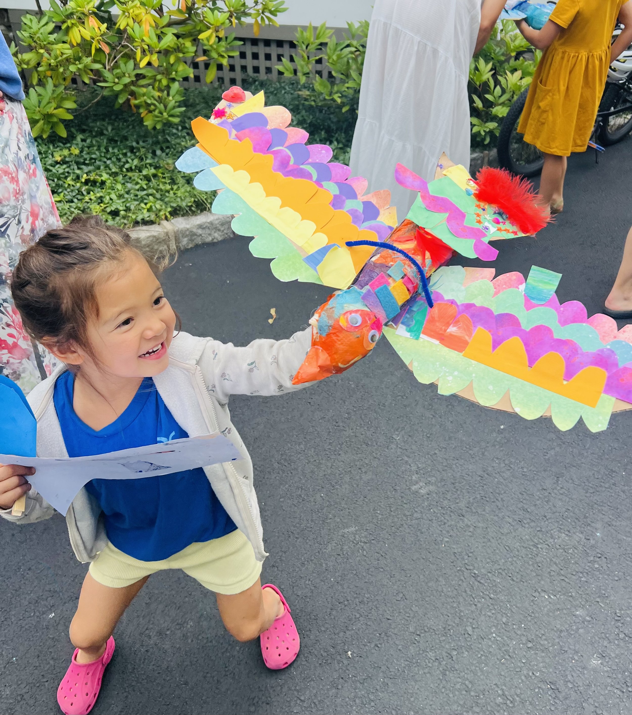 A young girl holding a colorful paper kite shaped like a dragon.