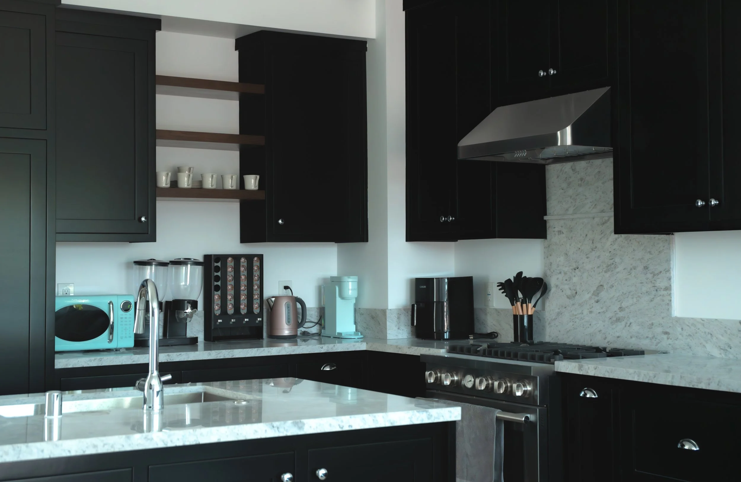 Modern kitchen with black cabinets, white marble countertops, stainless steel appliances, and various kitchen utensils and small appliances on the counter.