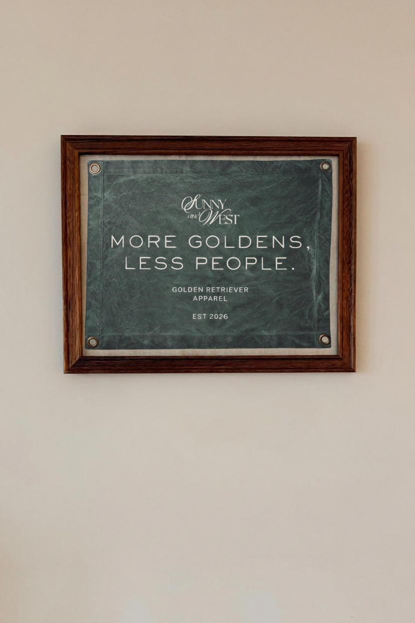 A framed sign on a wall that reads 'More Goldens, Less People' with additional text about golden retriever apparel and the year 2026.