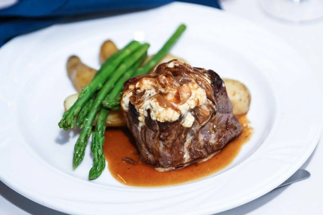 A plated meal featuring a beef steak topped with mushroom gravy, with green asparagus and roasted potato slices on the side.