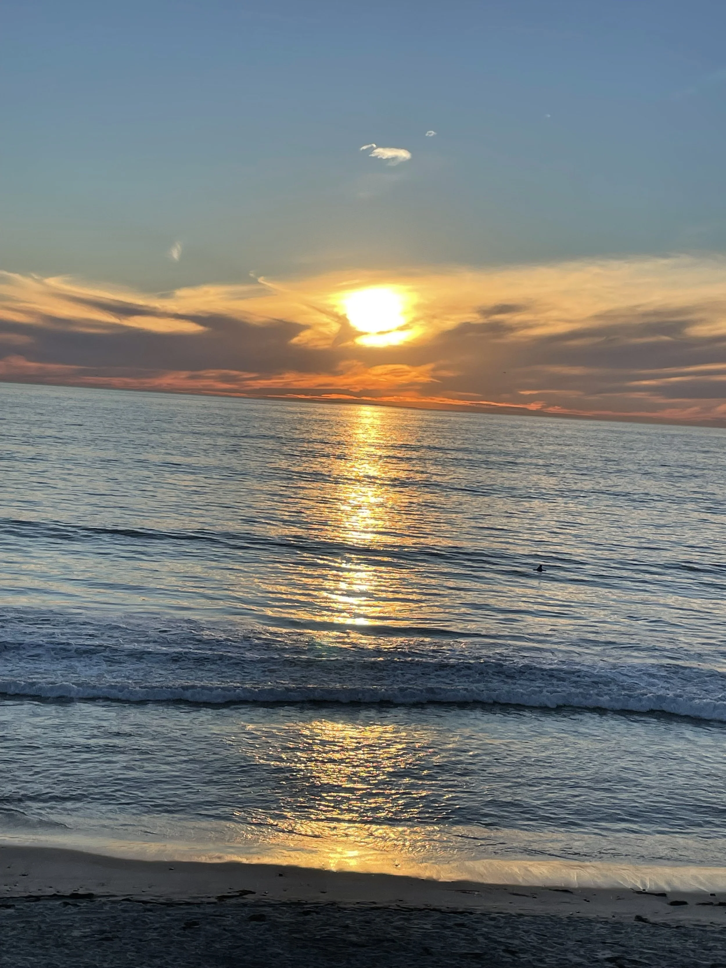Sunset over the ocean with reflections on the water and some clouds in the sky.