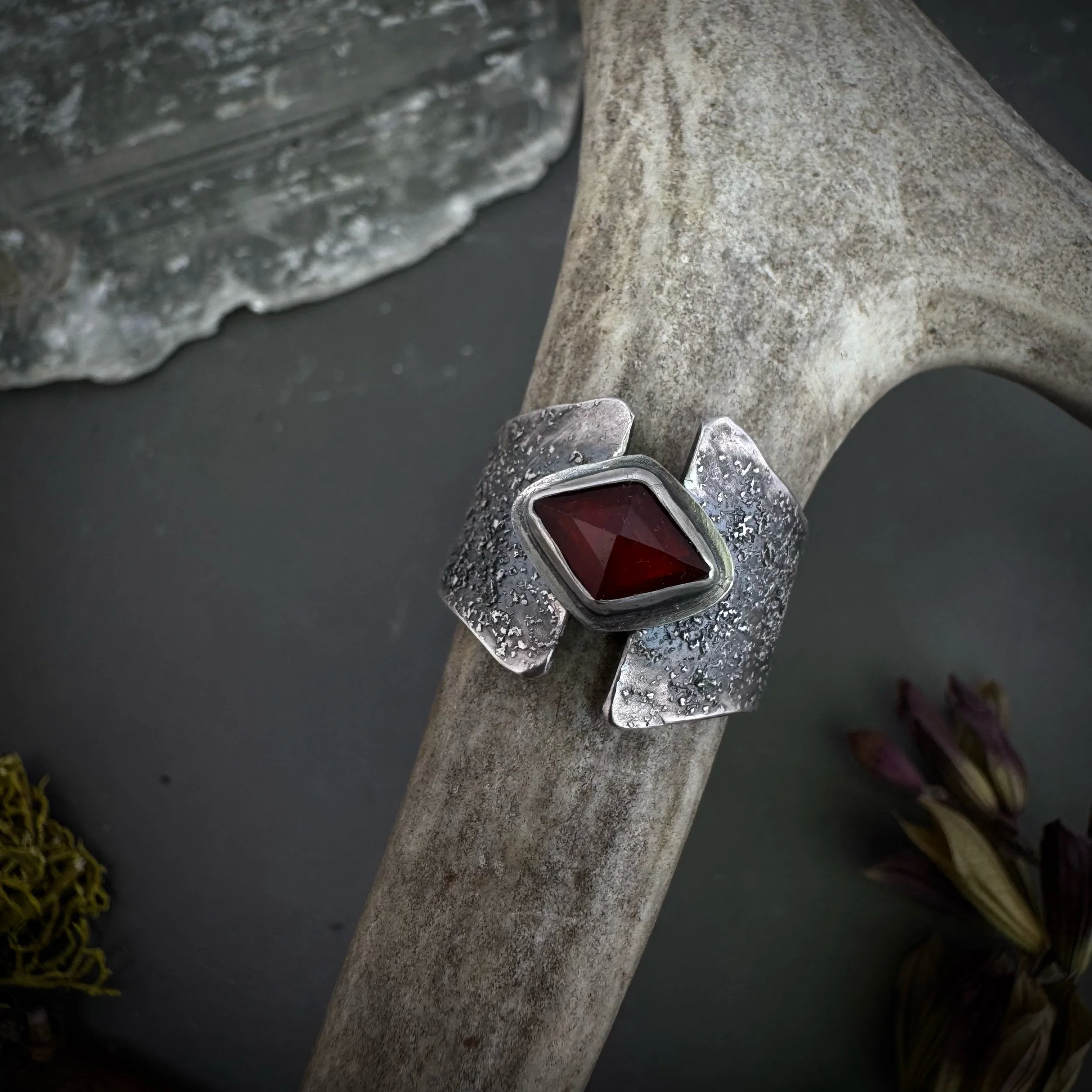 Sterling silver ring with kite-shaped garnet stone, silver dust texture, and stepped wing-like shoulders