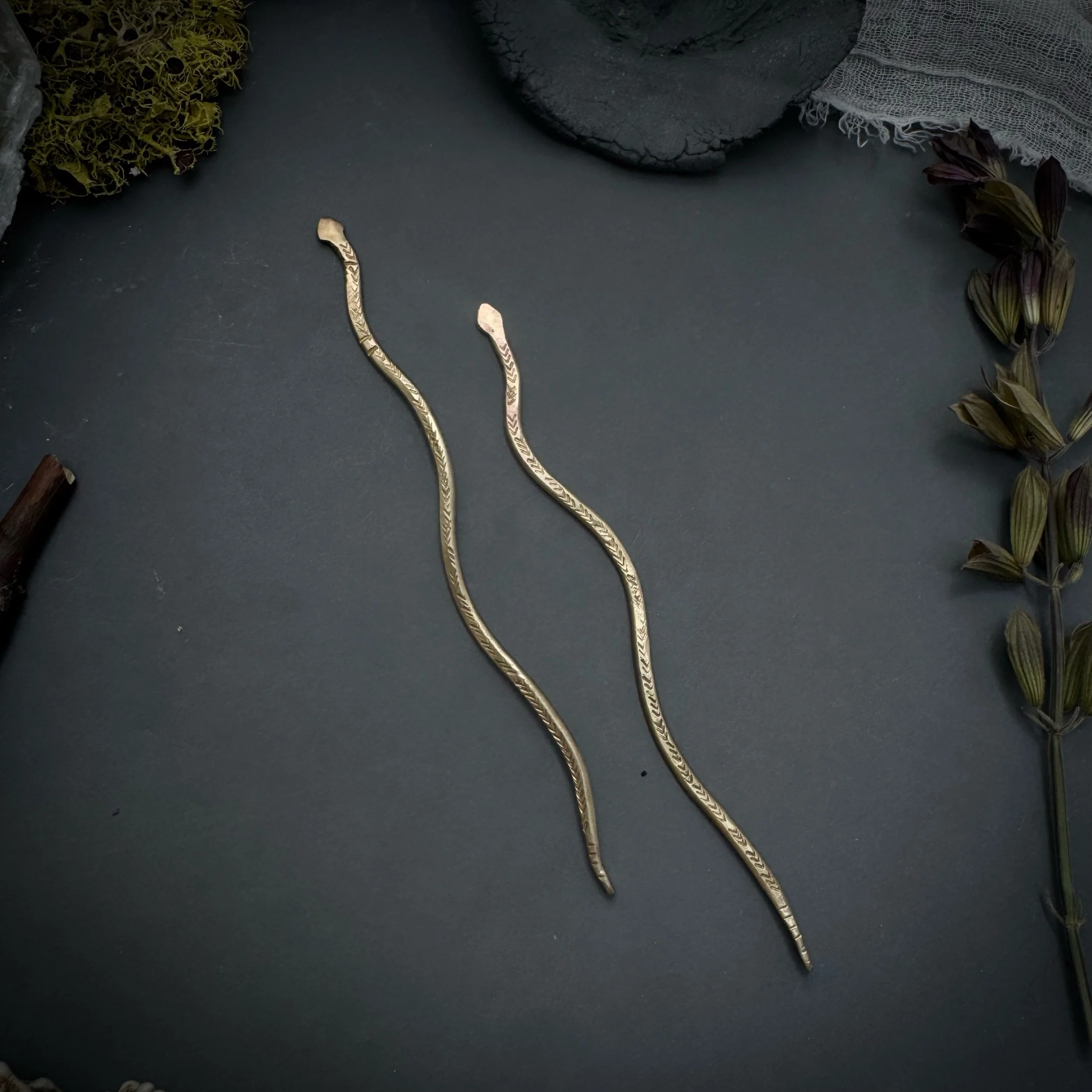Two hammered brass serpent-shaped hair sticks with textured detail