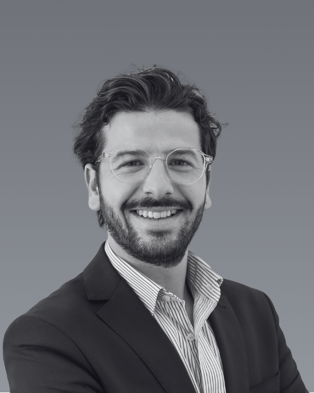 Portrait en noir et blanc d'Alexandre Viallet Nouhant souriant, portant des lunettes et un costume, avec une chemise à rayures, fond gris.