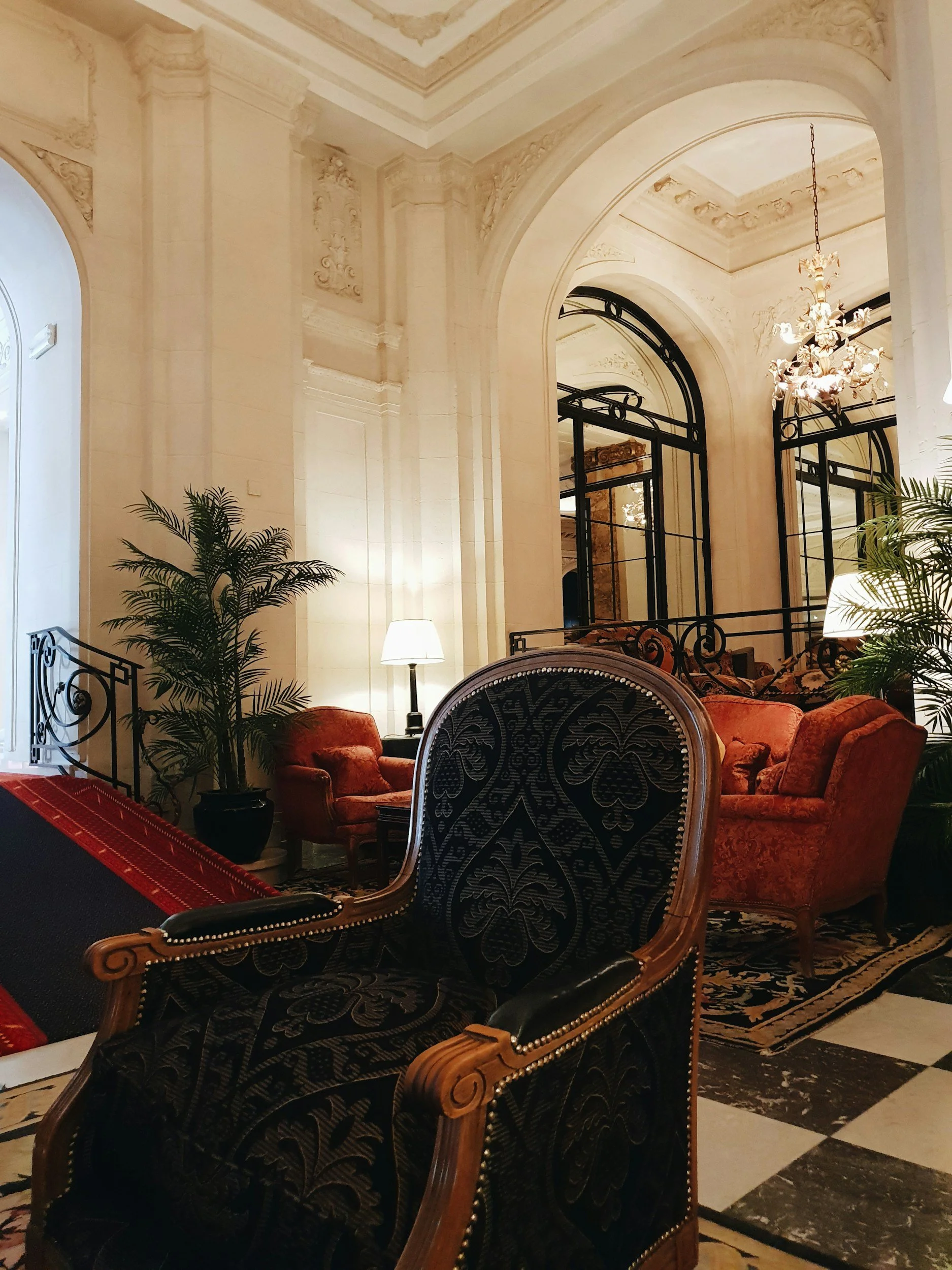 Intérieur d'un lounge d'hôtel à Paris, élégant avec des fauteuils en velours rouge, un miroir grand arqué, des plantes vertes, une lampe de table et un chandelier.