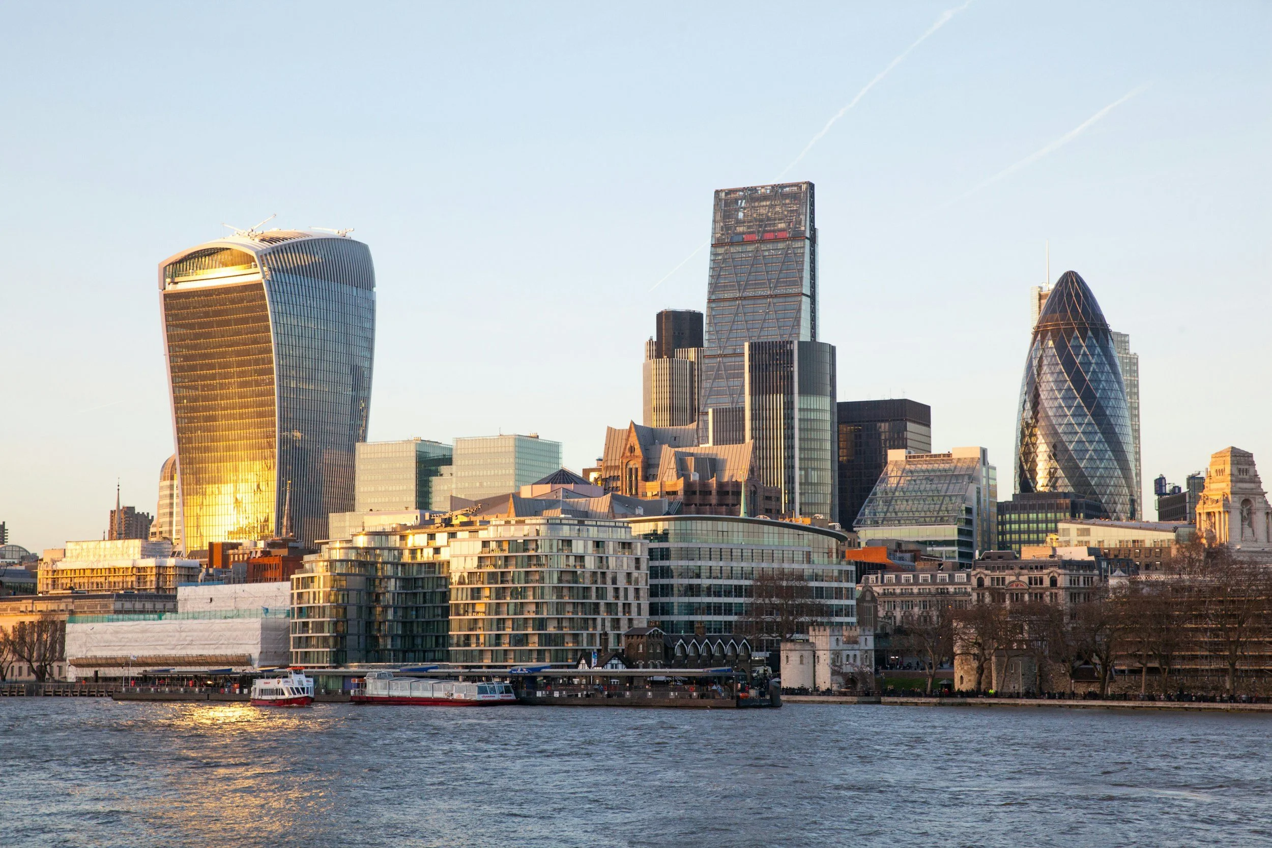 Vue de la ligne d'horizon de Londres avec des bâtiments modernes au bord de l'eau, notamment le 20 Fenchurch Street (Le Capital) et le 30 St Mary Axe (The Gherkin), sous un ciel clair.
