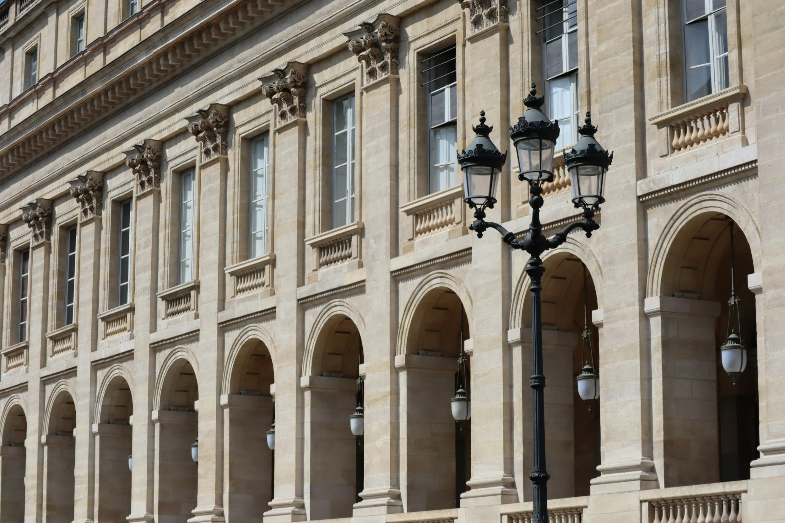 Facade en pierre d'un bâtiment historique avec fenêtres à fronton et balustrades, lampadaire en fer forgé au premier plan