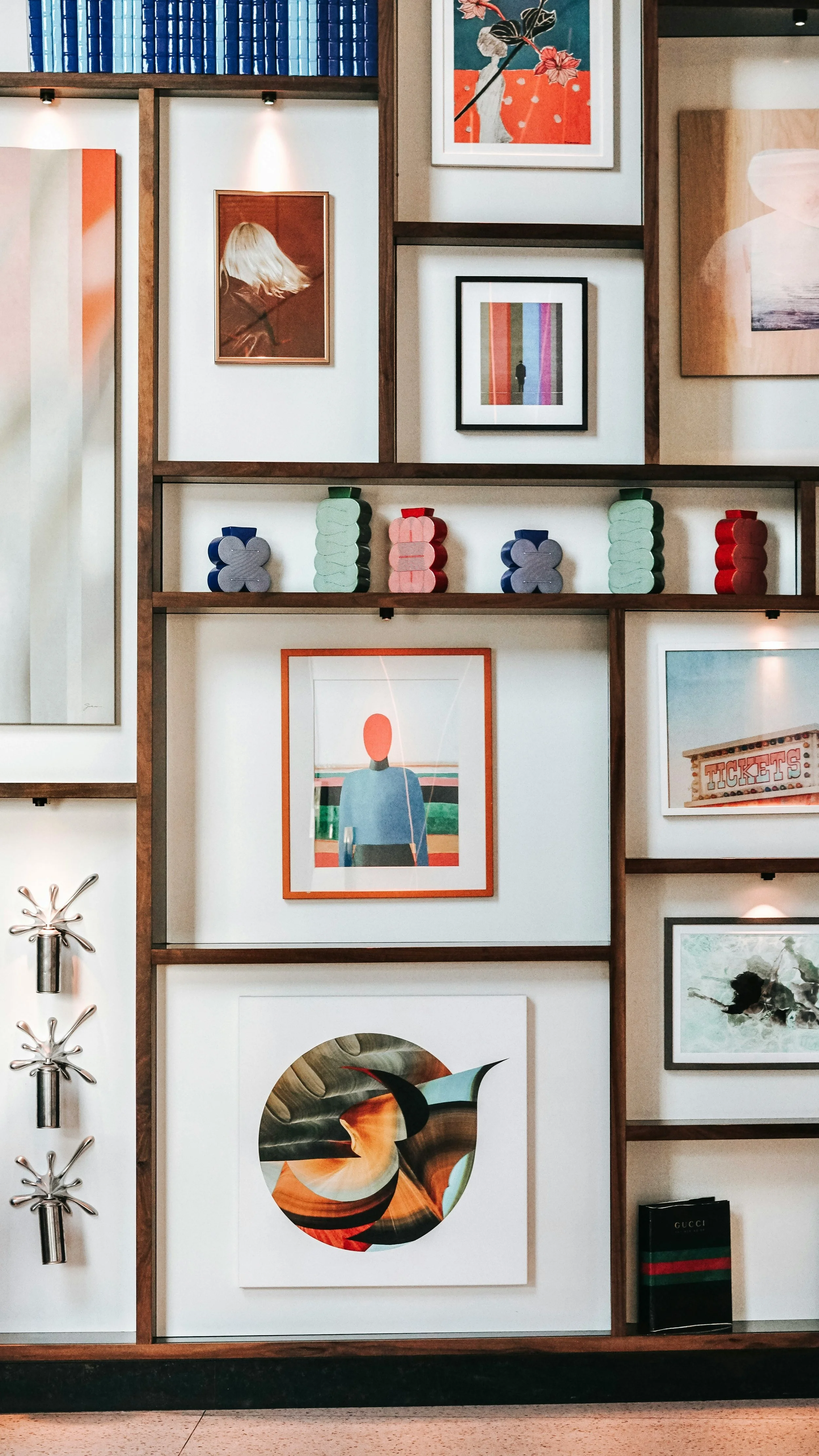 Une décoration murale avec plusieurs cadres d'art moderne et des coussins colorés suspendus sur une étagère.