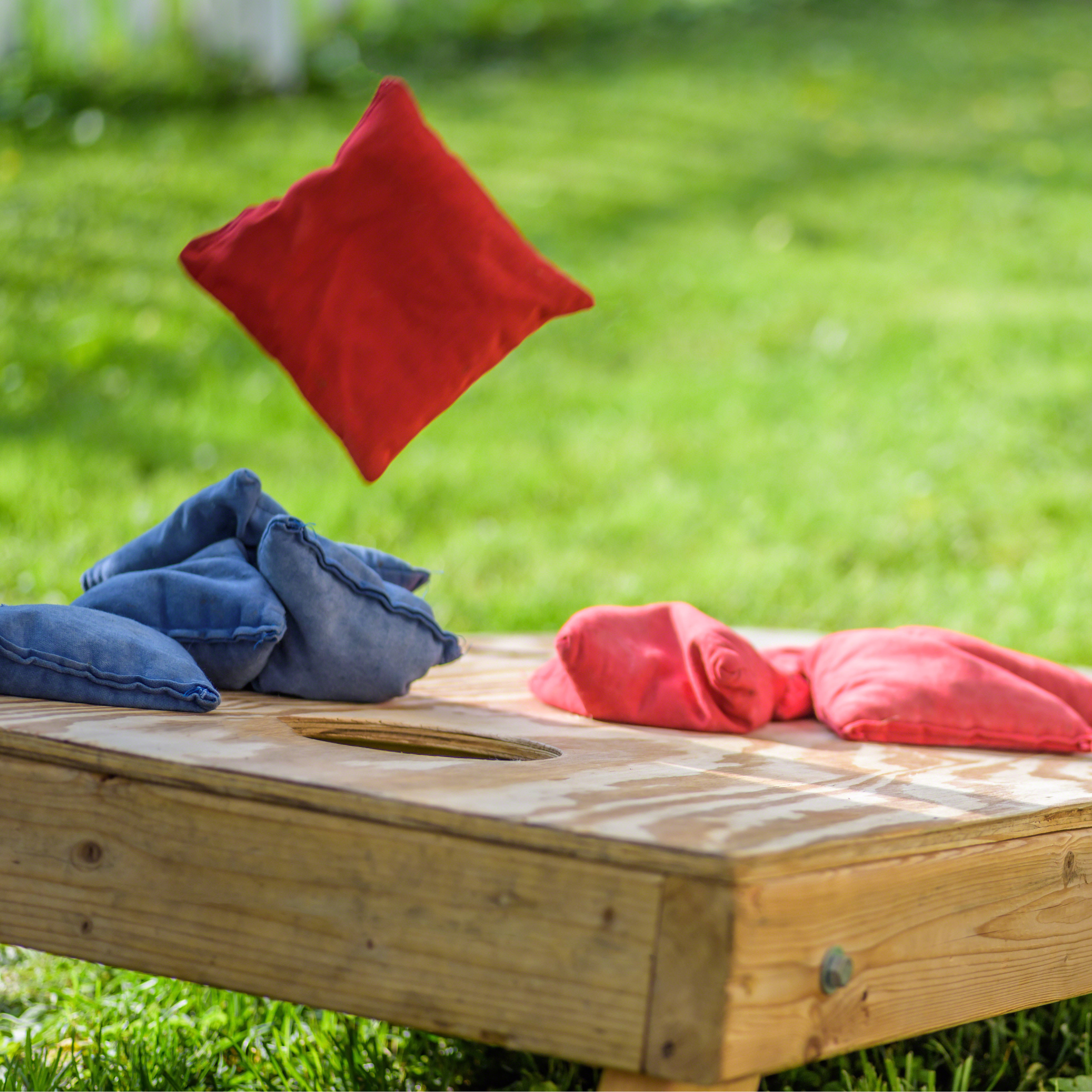 Colourful cloth bean bags being tossed into the air on a wooden surface outdoors with grass in the background.