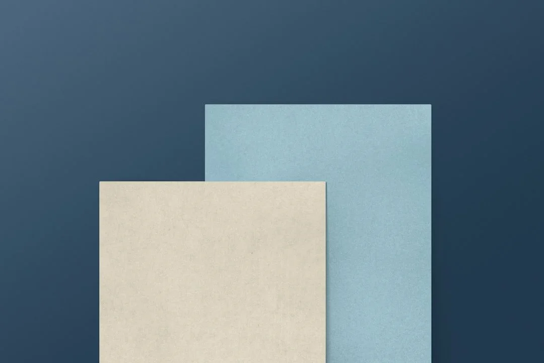 Two textured paper sheets, one beige and one light blue, positioned in front of a dark blue background.