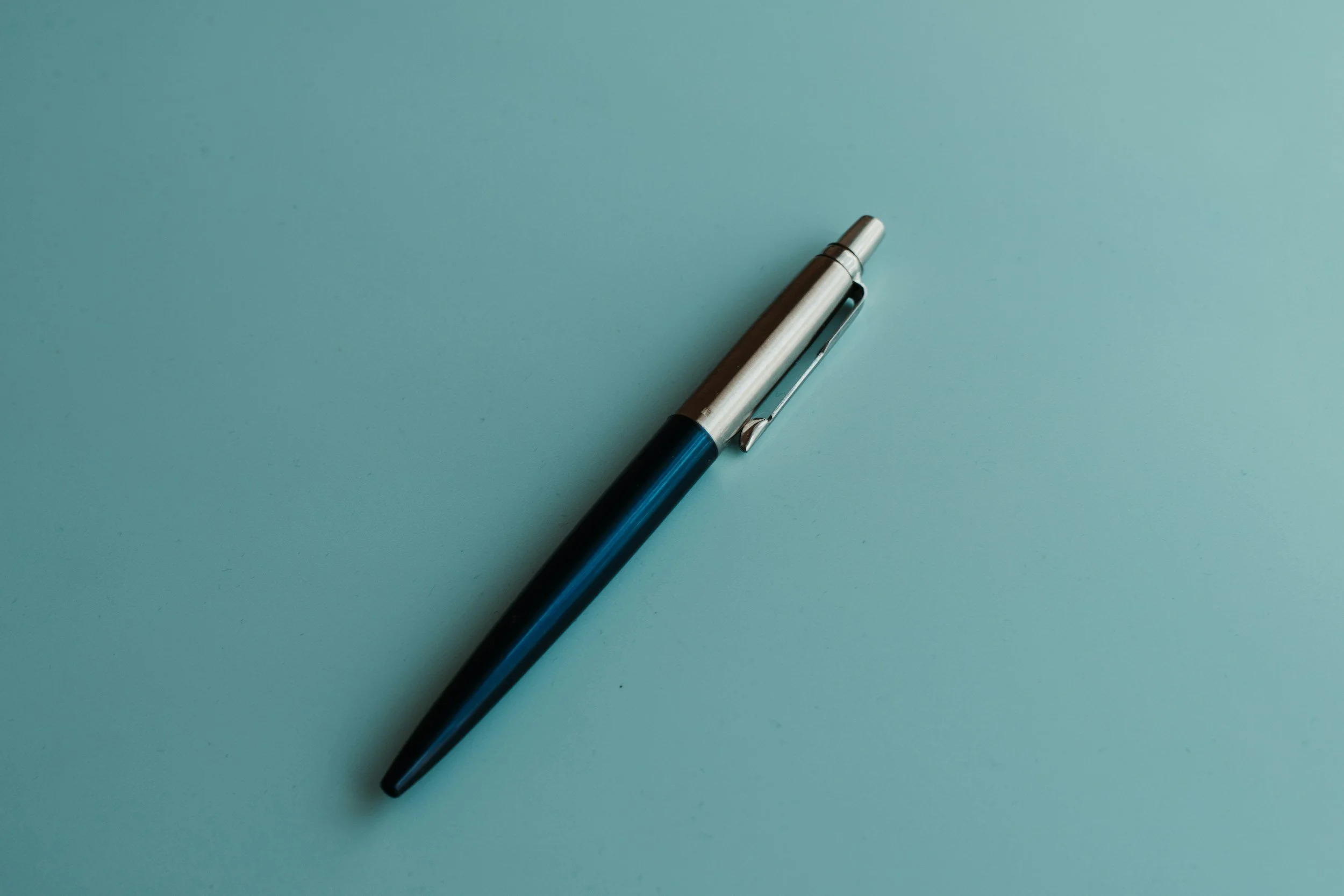 A black and silver pen with a clip, lying on a light blue surface.