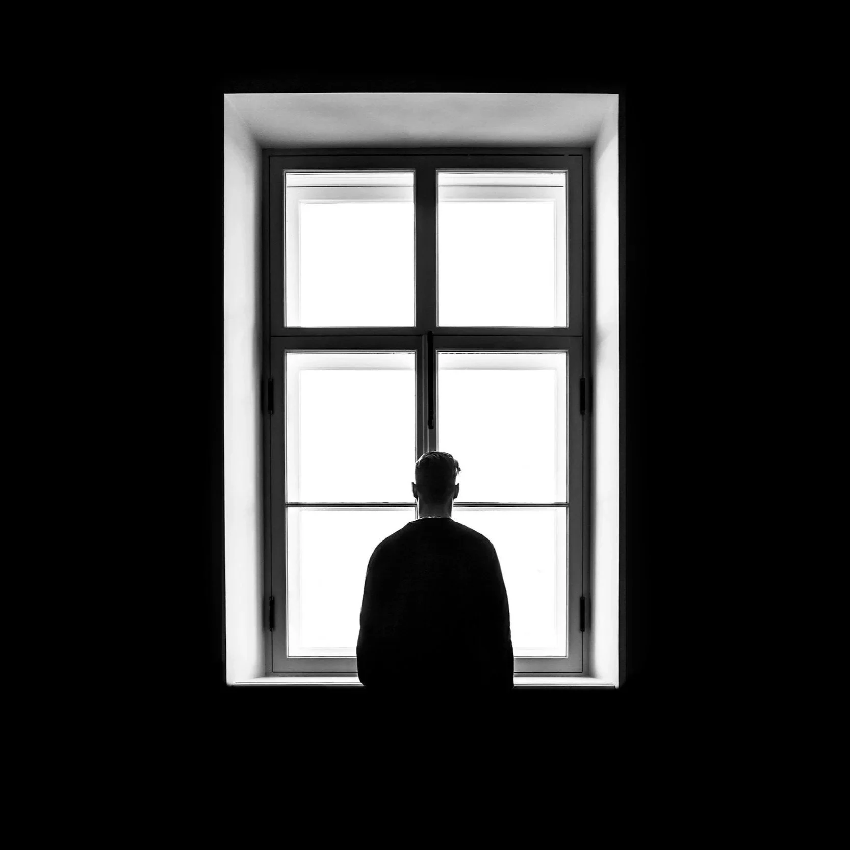 Person standing in front of a large window in a dark room, with only their silhouette visible.