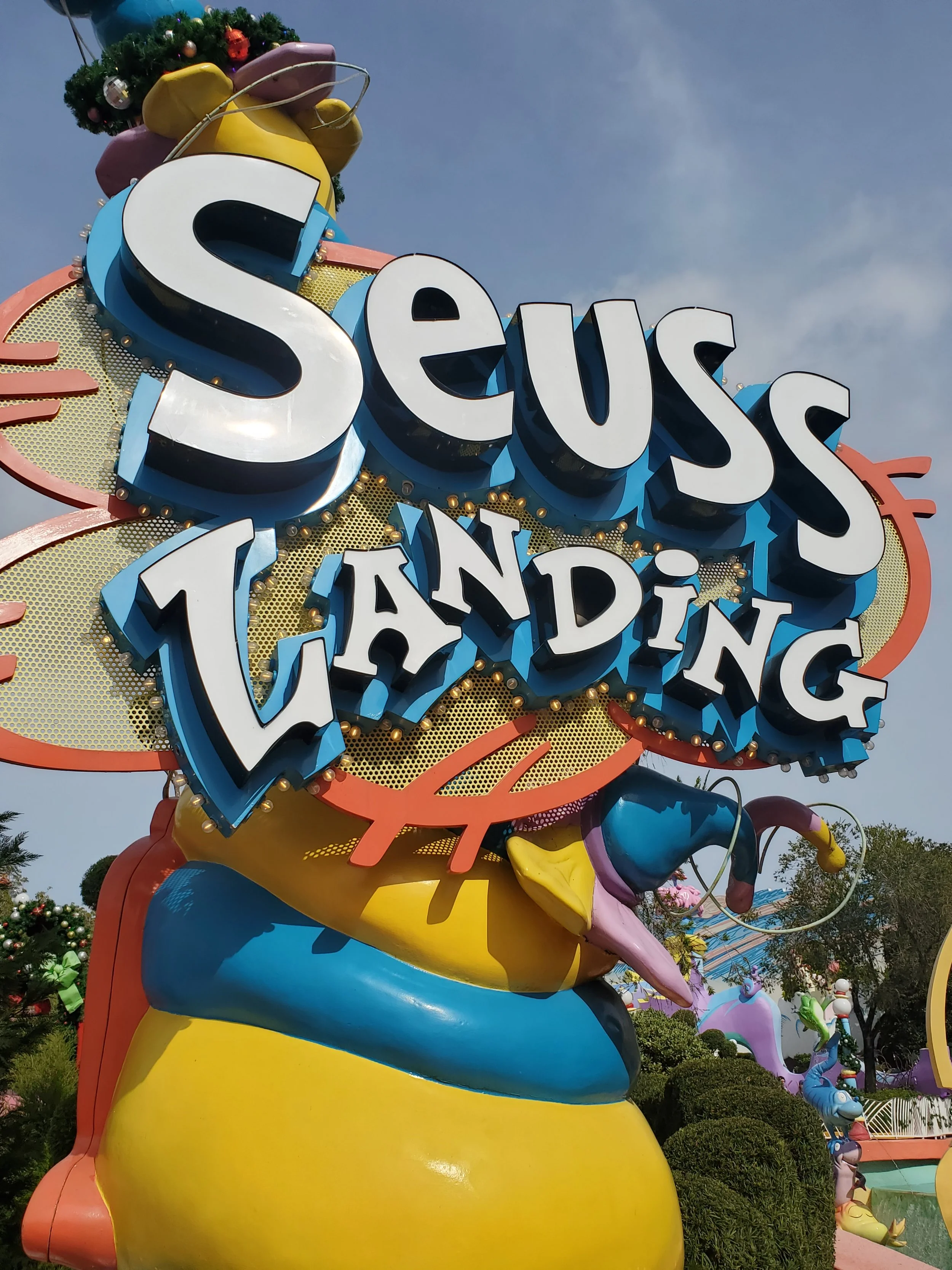 Colorful sign that says Suess Landing from Islands of Adventure in Universal Studios Orlando with a decorative background featuring large cartoonish lips and eyes, and a whimsical theme.