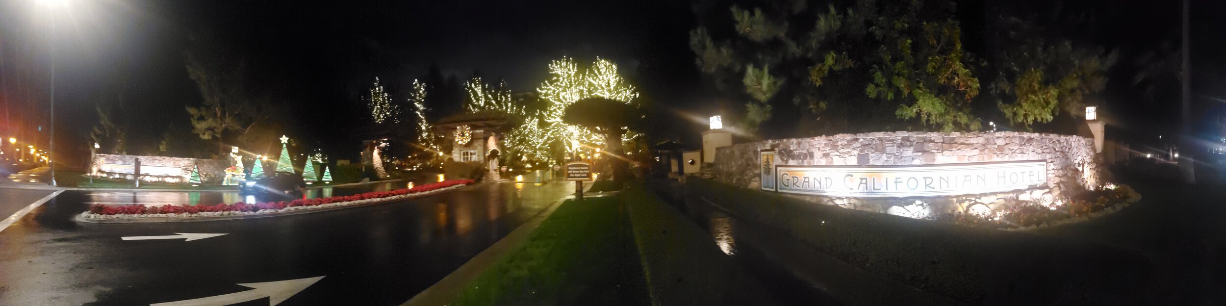 Night view of the entrance to the Grand Californian Hotel decorated with Christmas lights, trees, and holiday decorations.