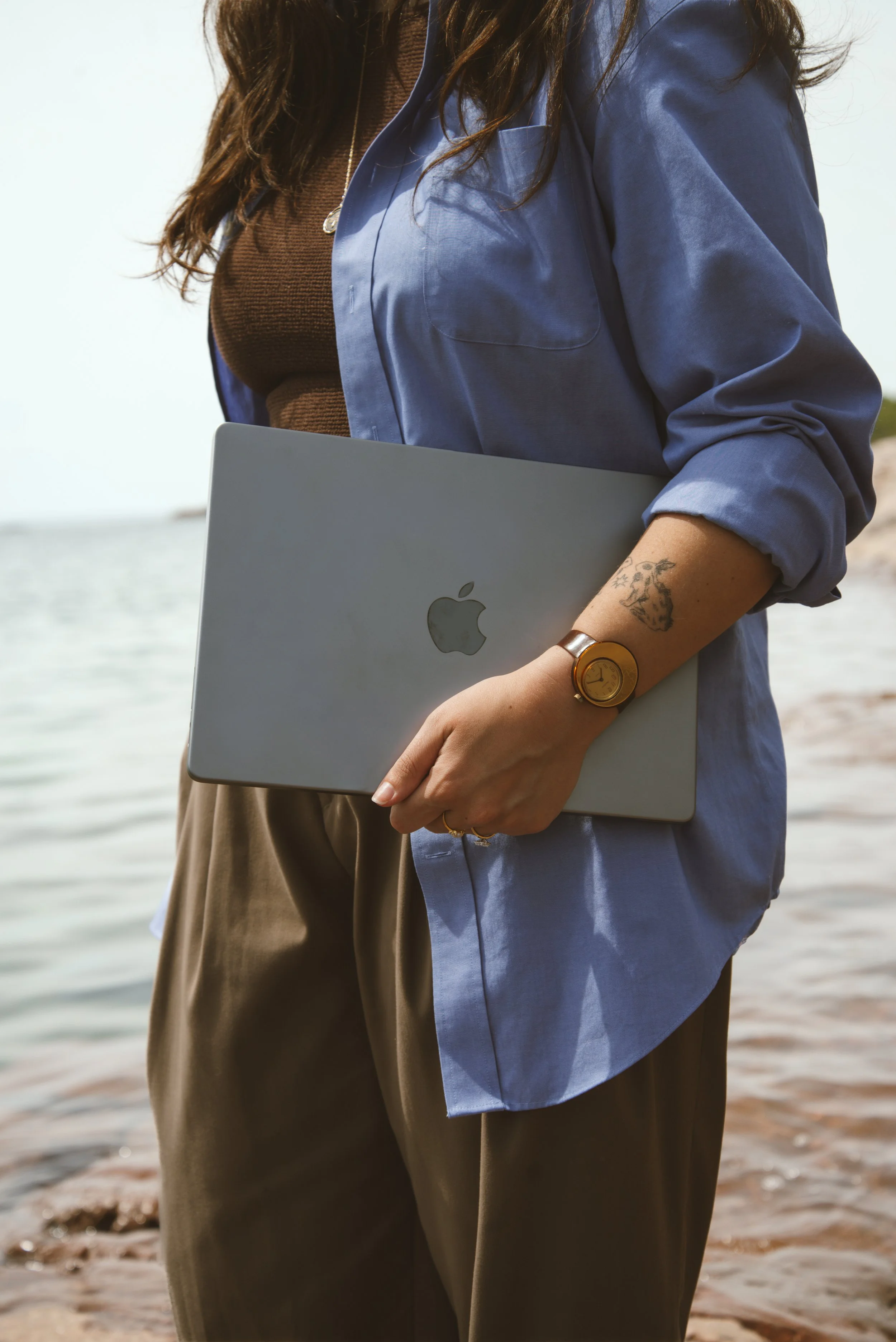 Designer holding MacBook with the apple facing outwards. The background is a blue lake.
