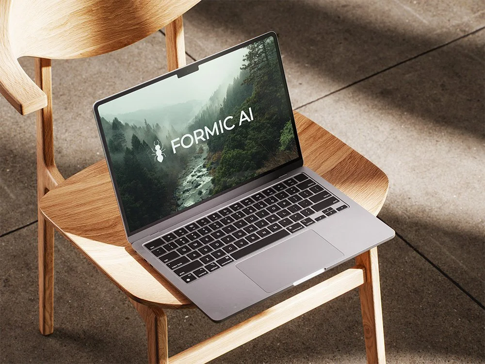 MacBook sitting on a chair with the logo FORMIC.AI as the screensaver