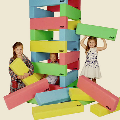 Three young girls playing with oversized, colorful foam building blocks arranged to look like a tower.
