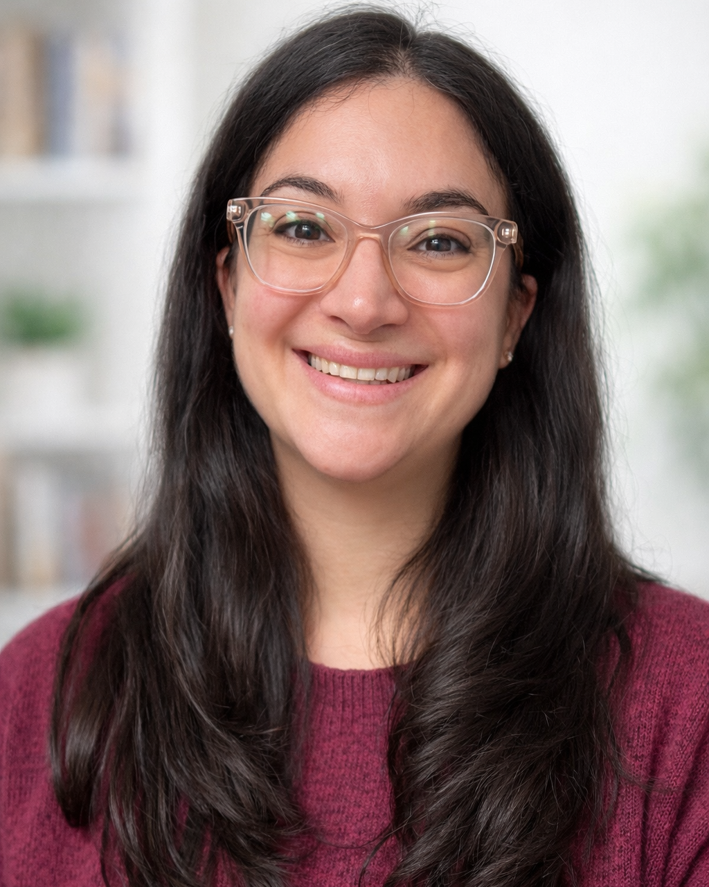A woman with long dark hair, glasses, and a maroon sweater smiling in an indoor setting.