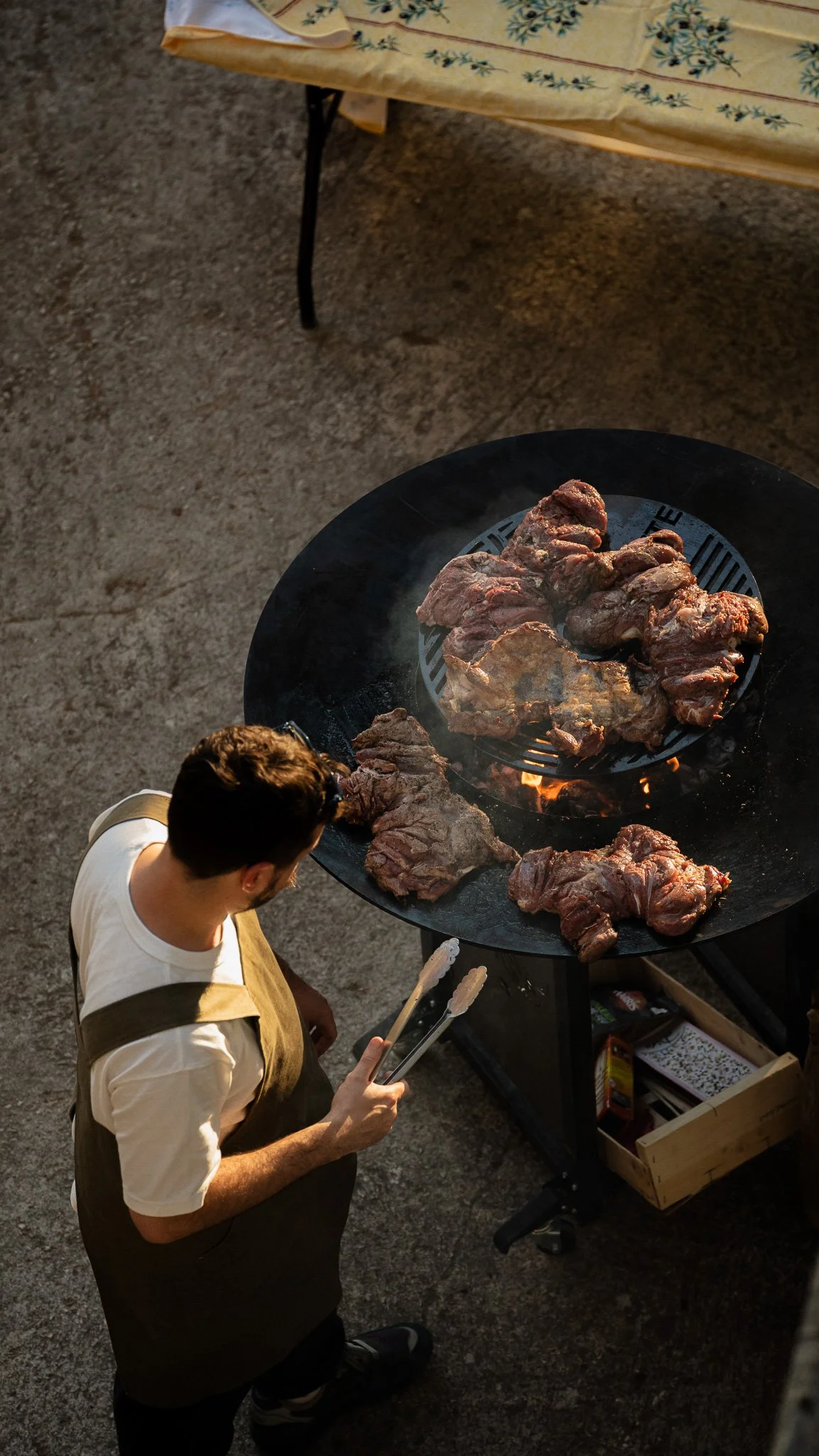 Un homme en train de cuire de la viande sur un gril circulaire lors d'un barbecue en plein air.