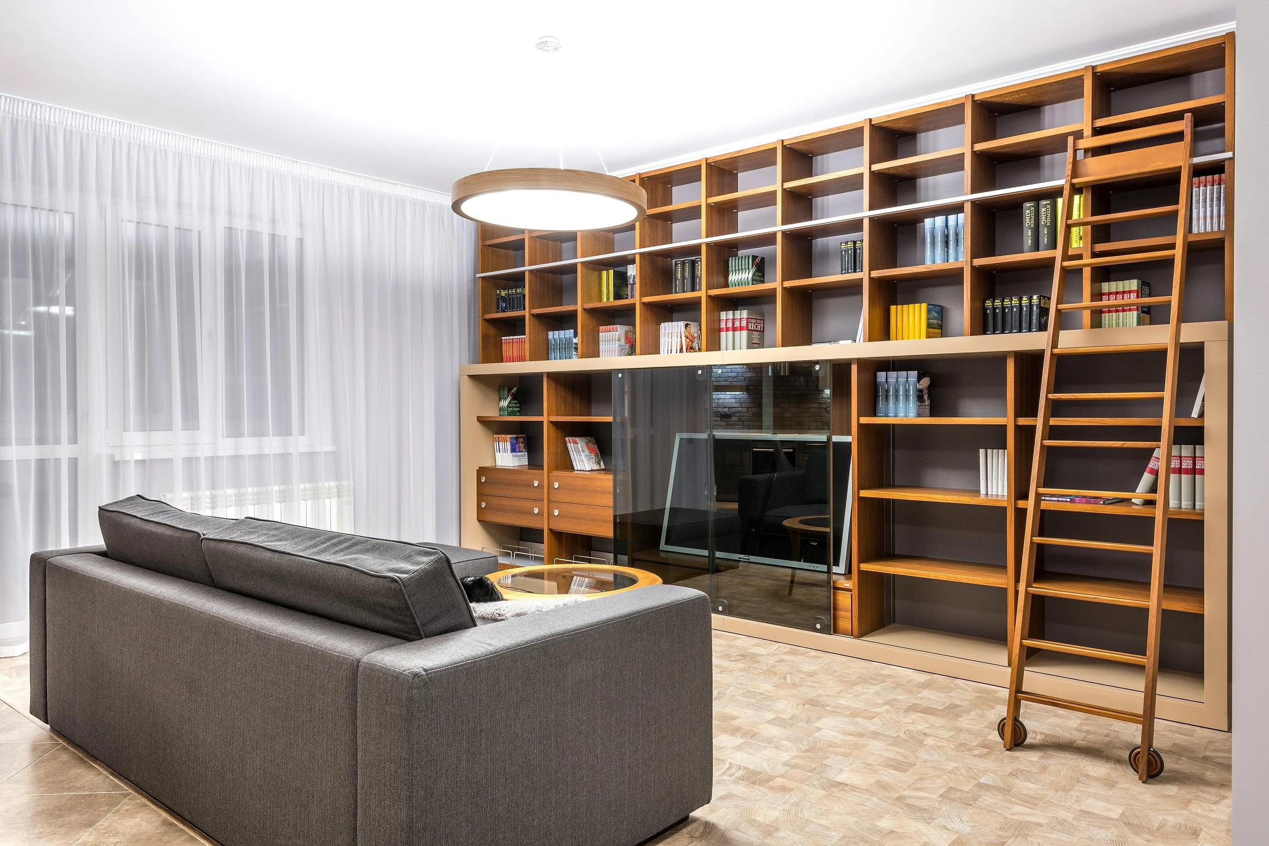 Living room with gray sofa and large wooden bookshelf, ladder, TV, and round ceiling light.