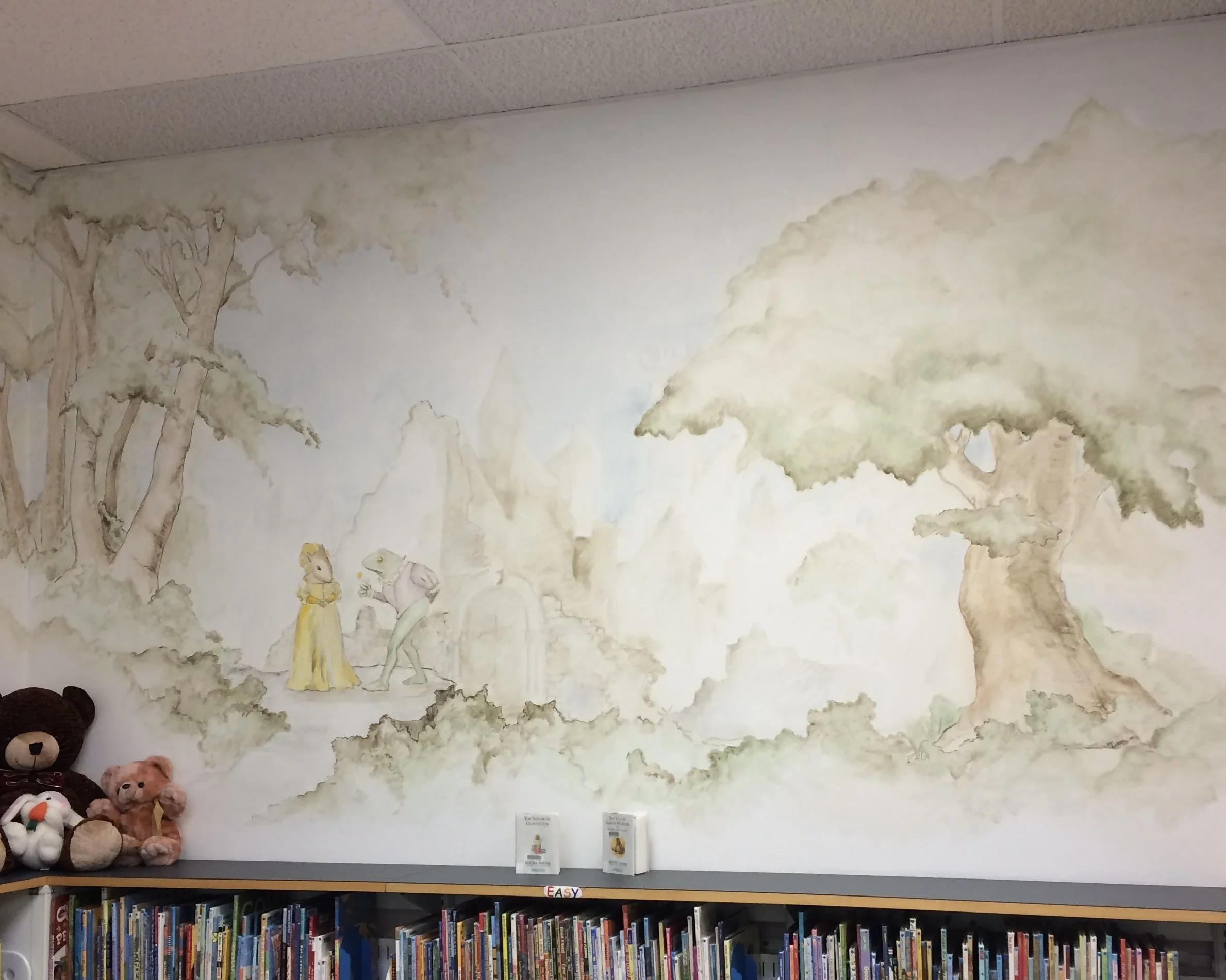 A wall mural of trees and clouds above a bookshelf filled with children's books. Teddy bears and stuffed animals are on a low shelf to the left.