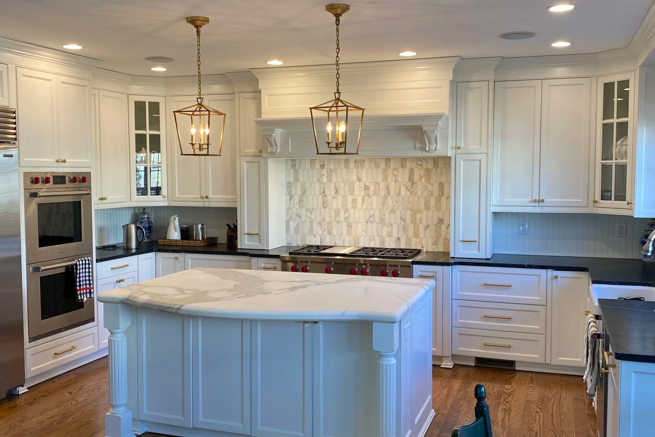 Modern kitchen with white cabinets, black countertops, marble island, and gold hardware, illuminated by two pendant lights.
