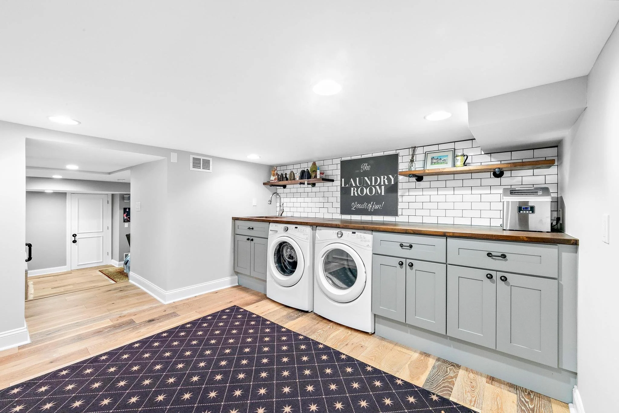 Laundry room with gray cabinets, subway tile backsplash, wooden countertop, and a black sign reading 'The Laundry Room Loads of Fun!', 