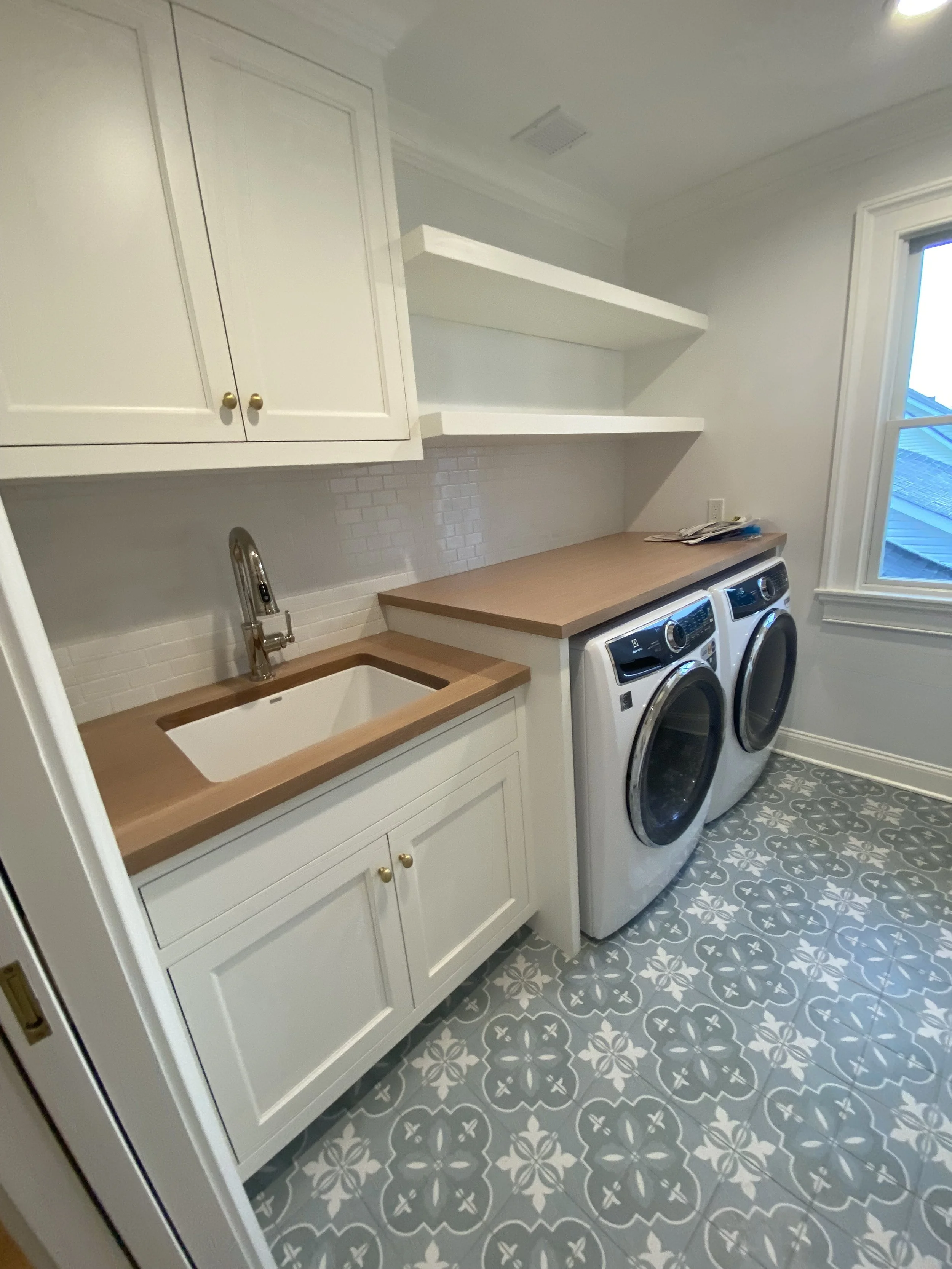 Laundry room with white cabinets, open shelving, a wooden countertop and beautiful patterned floor tiles.